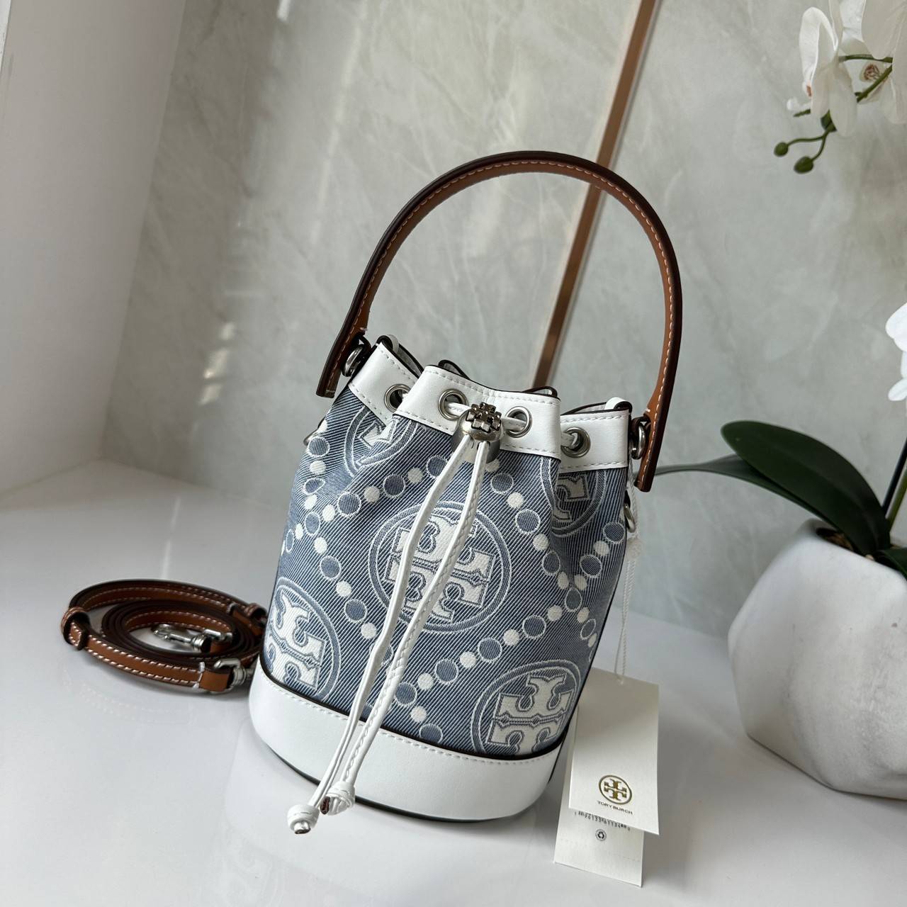 TORY BURCH Mini T Monogram Denim Bucket Bag คอลเลคชั่นใหม่ รูปแบบคลาสสิค พกพาความหรูหราไปได้ทุกที่ด้วยกระเป๋าทรง Bucket ขนาดกลางและปิดด้วยเชือกรูดพร้อมโลโก้แวววาว วัสดุผ้าเดนิมแจ็คการ์ด ตัดขอบหนังแท้ สวยหรู ทันสมัยสุดๆคะ