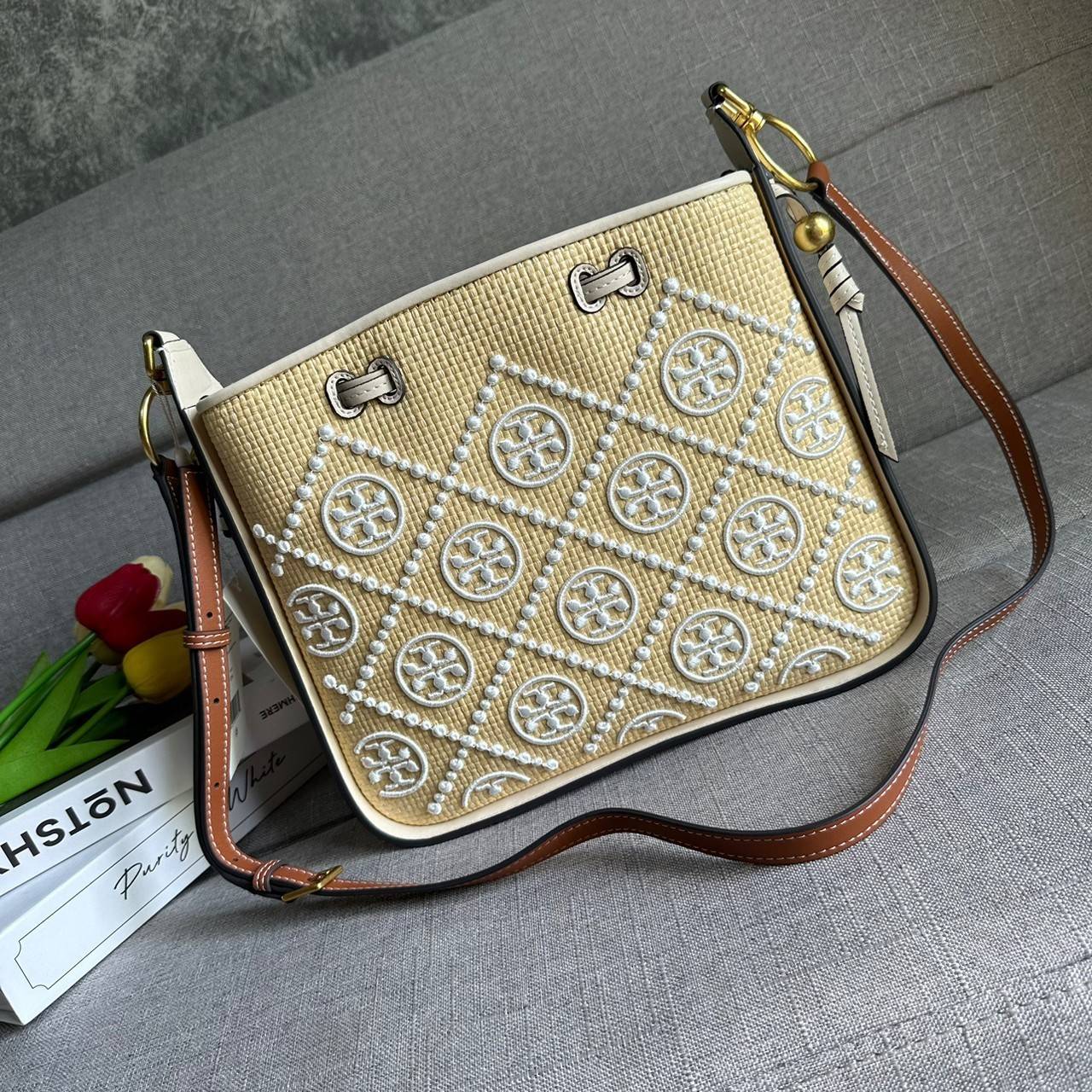 TORY BURCH T Monogram Straw Bell Bag กระเป๋าสะพายข้างรุ่นคลาสสิกที่ได้แรงบันดาลใจจากการควิลท์แบบดั้งเดิมของเพนซิลเวเนีย คอลเลกชันบ่งบอกถึงความมีสไตล์เหนือกาลเวลา รูปทรงเรียวโดดเด่น ปักทอลายแบรนด์อย่างสวยงาม เปิด ปิดด้วยเชือกรูด ด้านในช่องโล่งกว้าง ซับในผ้