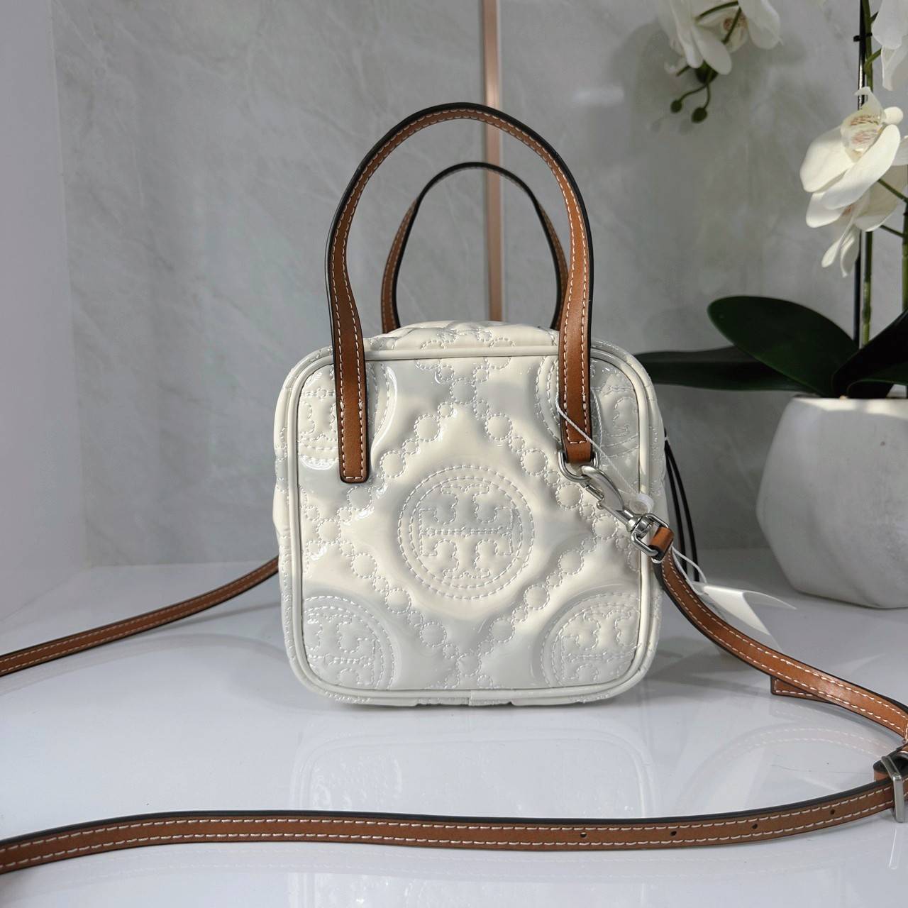 Tory Burch T Monogram Embroidered Patent Cube คอลเลคชั่นใหม่ รุ่นลิมิเต็ดรูปทรงใหม่ T Monogram สุดcube วัสดุหนังแท้ เปิด-ปิดด้วยซิป ภายในกว้าง มีช่องแยก 1 ช่อง สามารถใส่โทรศัพท์มือถือได้ทุกรุ่น สามารถถือหิ้วหรือสะพายได้ สายสามารถถอดและปรับระดับได้คะ