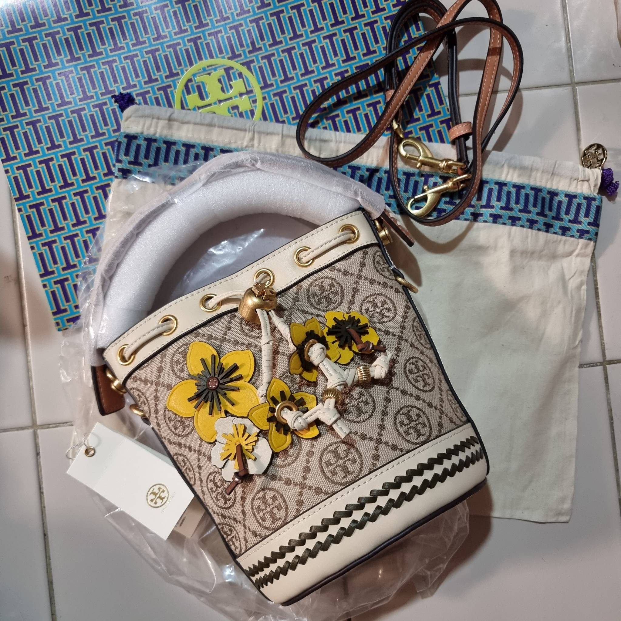TORY BURCH MINI T MONOGRAM FLORAL BUCKET BAG คอลเลคชั่นใหม่ พร้อมเสิร์ฟความสวยให้ถึงบ้าน!! กระเป๋าบัคเก็ตทรงยอดนิยม ไซส์มินิ ดีไซน์ใหม่ล่าสุด สไตล์งานคราฟ มีลูกเล่นประดับดอกไม้กับตัวกระเป๋า และตัวรูดสาย วัสดุผ้า jacquard ตัดสลับหนังแท้ หูจับและขอบกระเป๋าต