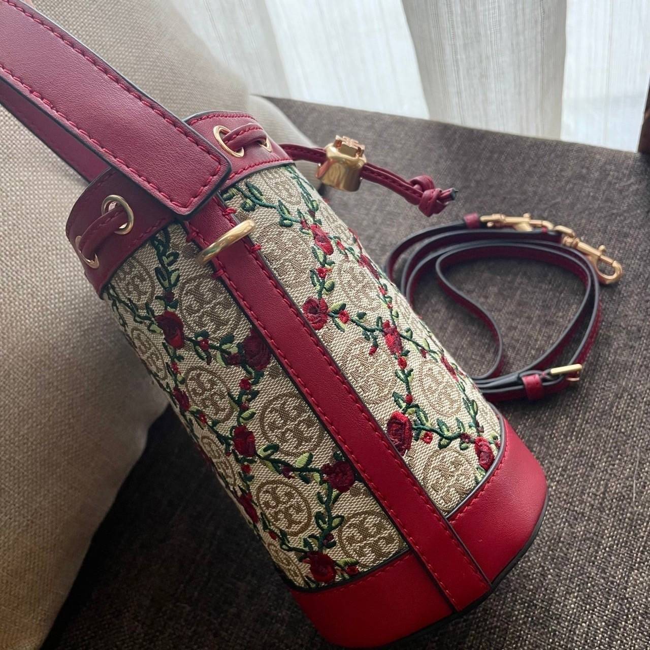 Mini : Tory Burch T Monogram Embroidered Mini Bucket Bag Hazelnut กระเป๋าทรงถังขนาดเล็ก เป็นแพทเทิร์นคลาสสิคที่ได้รับแรงบันดาลใจจากการควิลท์แบบดั้งเดิมของเพนซิลเวเนีย คอลเล็คชั่นบอกเล่าความมีสไตล์เหนือกาลเวลา ลายดอกกุหลาบสีแดงลายปักษ์ วัสดุผ้าสว๊อตซ์วินเท