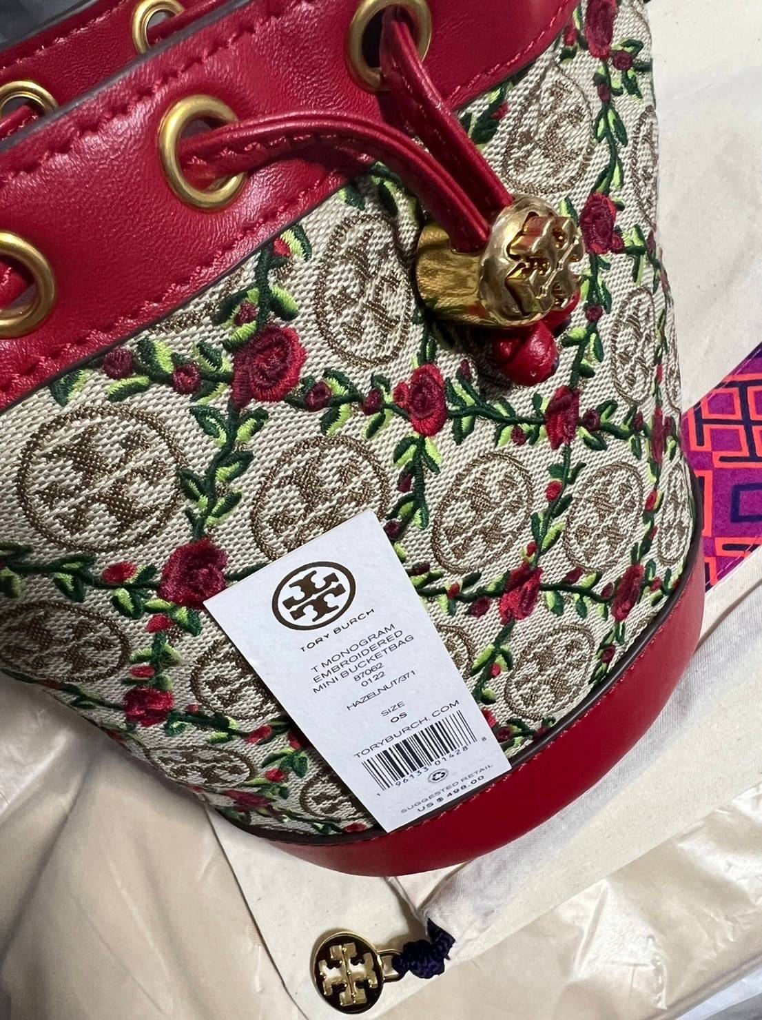 Mini : Tory Burch T Monogram Embroidered Mini Bucket Bag Hazelnut กระเป๋าทรงถังขนาดเล็ก เป็นแพทเทิร์นคลาสสิคที่ได้รับแรงบันดาลใจจากการควิลท์แบบดั้งเดิมของเพนซิลเวเนีย คอลเล็คชั่นบอกเล่าความมีสไตล์เหนือกาลเวลา ลายดอกกุหลาบสีแดงลายปักษ์ วัสดุผ้าสว๊อตซ์วินเท