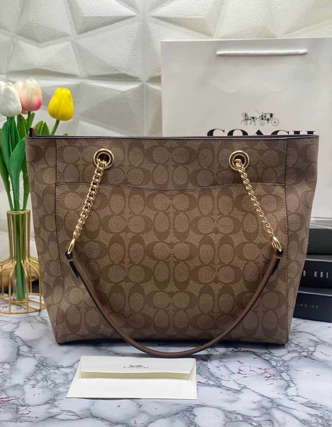 COACH Tote in Signature Canvas Bag กระเป๋าสะพายทรงช้อปปิ้ง สายกระเป๋าเป็นหนังสลับโซ่ทองสวยงาม เพิ่มความหรูหรา ภายในโล่งกว้างใส่ของได้เยอะมาก วัสดุ Canvas เคลือบลายซิกเนเจอร์และหนัง พร้อมซิปกลางเก็บของได้มิดชิดเลยค่ะ มี 3 สี น้ำตาล ดำ ขาว