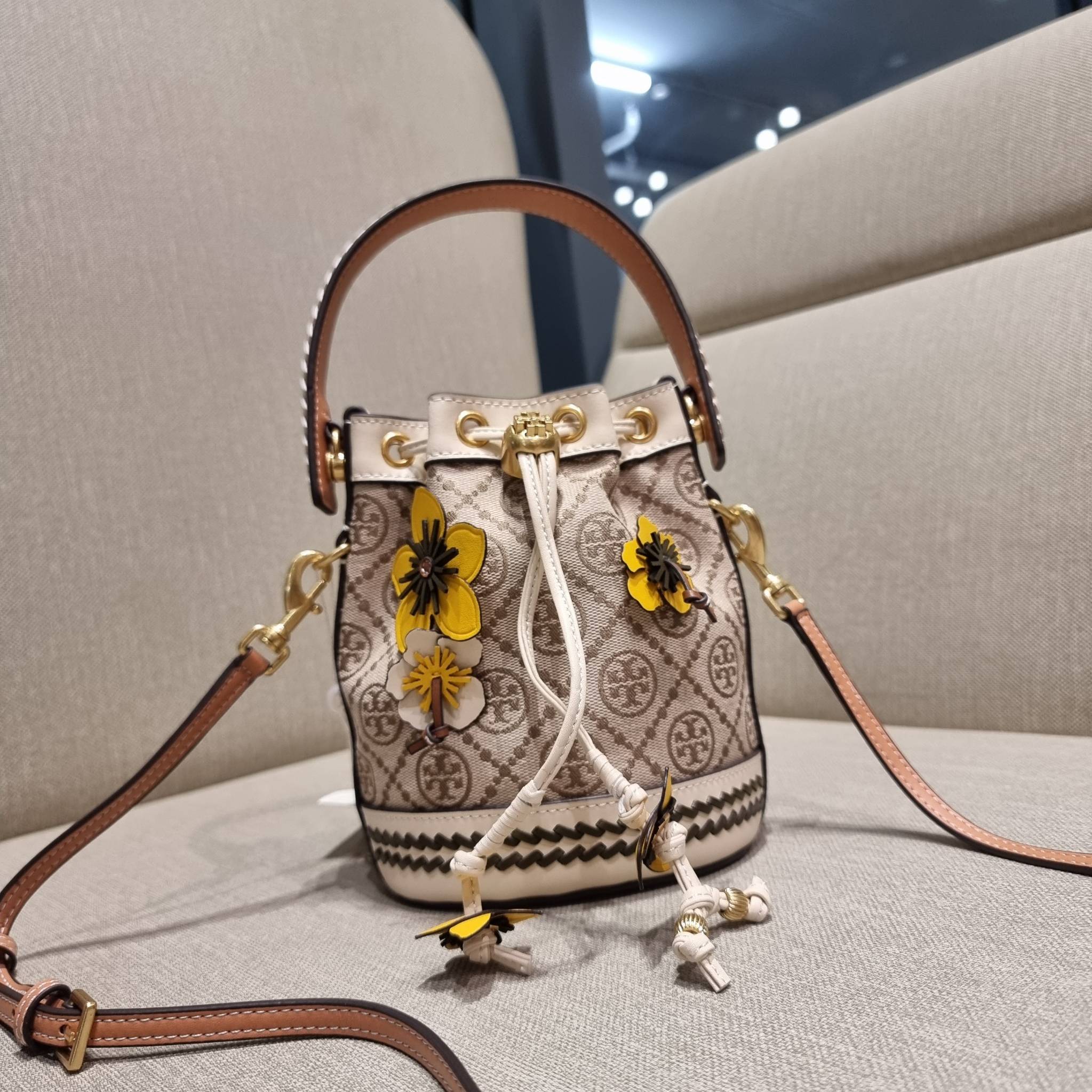 TORY BURCH MINI T MONOGRAM FLORAL BUCKET BAG คอลเลคชั่นใหม่ พร้อมเสิร์ฟความสวยให้ถึงบ้าน!! กระเป๋าบัคเก็ตทรงยอดนิยม ไซส์มินิ ดีไซน์ใหม่ล่าสุด สไตล์งานคราฟ มีลูกเล่นประดับดอกไม้กับตัวกระเป๋า และตัวรูดสาย วัสดุผ้า jacquard ตัดสลับหนังแท้ หูจับและขอบกระเป๋าต