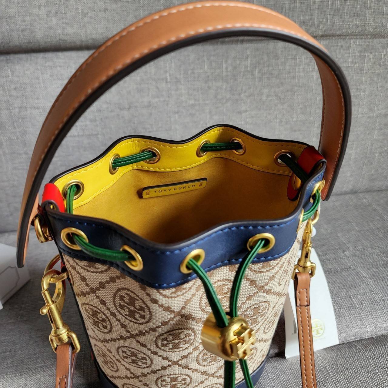 TORY BURCH T MONOGRAM COLORBlOCK JACQUARD MINI BUCKET BAG คอลเลคชั่นใหม่ล่าสุด ครอบครองก่อนใคร รุ่นบัคเก็ตทรงจีบ วัสดุ jacquard สลับหนังแท้ ตัดขอบข้างสีแดงทำให้ดูโดดเด่น หูจับหนังแท้ เปิด ปิด แบบหูรูด ภายในช่องโล่งกว้าง มาพร้อมสายสะพายข้างหนังแท้ ปรับระดั