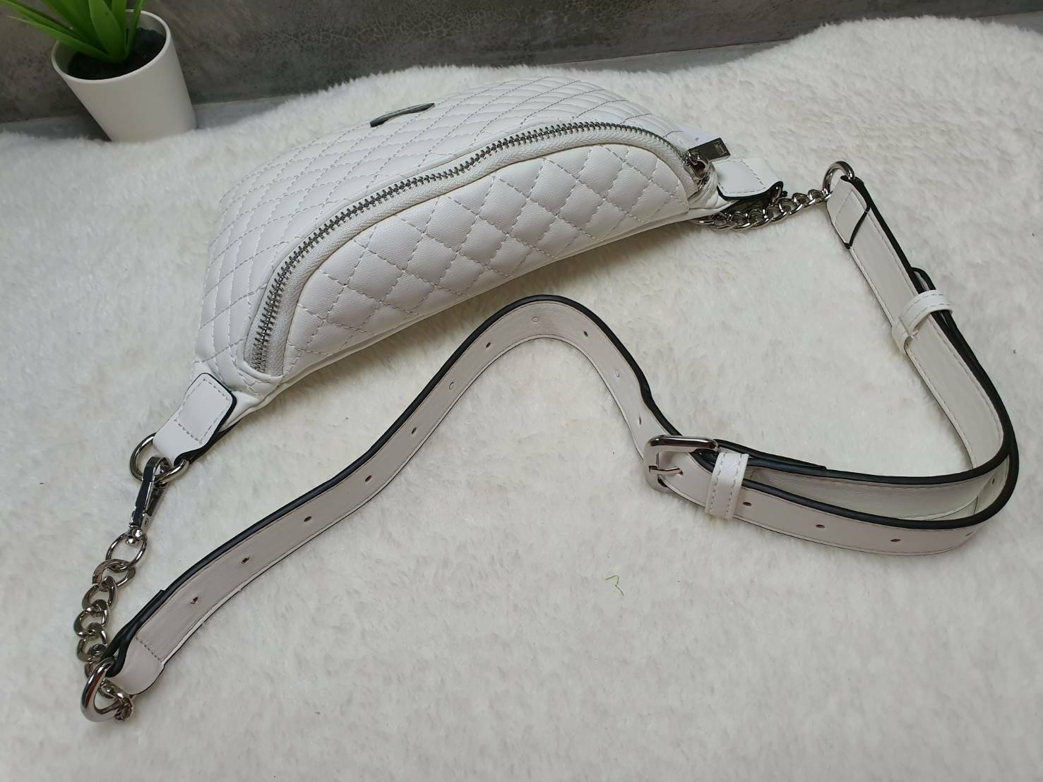 กระเป๋า Guess รุ่นนี้คาดเอว/คาดอก/สะพายข้างได้ครบทุกฟังก์ชั่น ด้านหน้าหนังเป็นลายตาราง ติดโลโก้แบรนด์รูปสามเหลี่ยมด้านหน้า เปิดปิดด้วยซิปยาว ด้านในเป็นช่องกว้างมีช่องซิปด้านใน ตัวกระเป๋าด้านหลังเป็นหนังเรียบ รุ่นนี้มีสายสะพายมา 2 เส้น เส้นแรกเป็นสายหนังปร