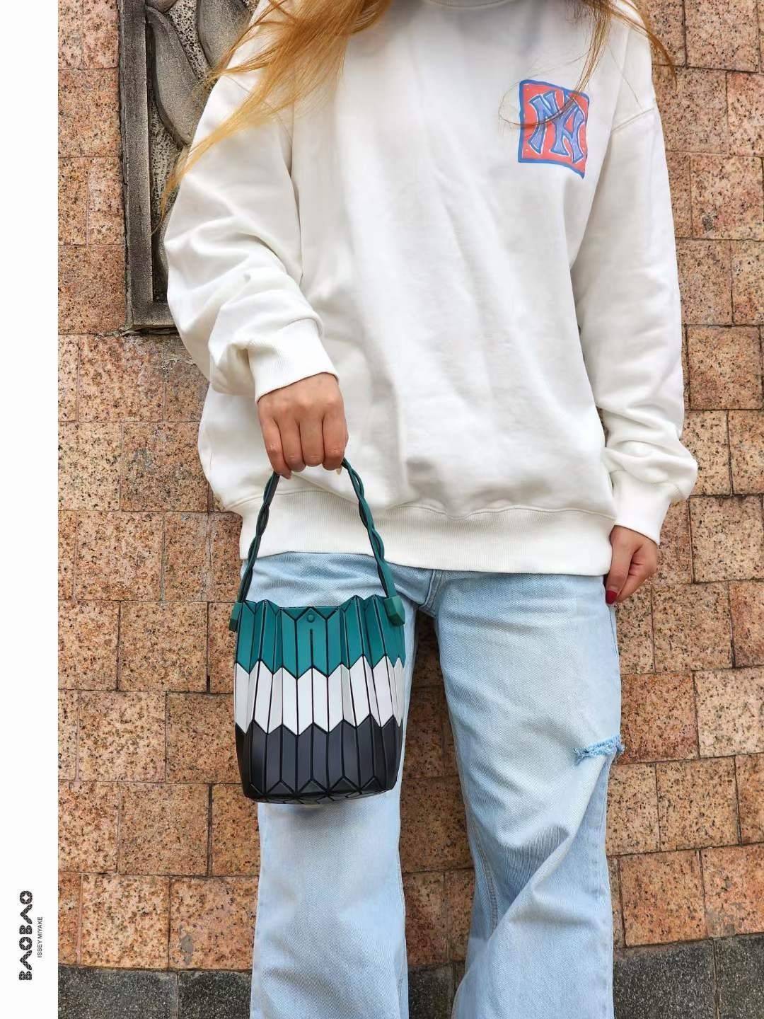 Small : BAO BAO ISSEY MIYAKE SMALL BUCKET เป็นกระเป๋าบัคเก็ตขนาดเล็กสามารถใช้ใส่กระเป๋าสตางค์และโทรศัพท์มือถือได้ ซีรีย์ใหม่นี้มีจุดเด่นที่แผ่นรูปทรงสี่เหลี่ยมด้านขนานในแนวตั้ง เกิดเป็นรูปทรงสามมิติซึ่งแตกต่างไปจากรูปทรงที่เกิดขึ้นจากแผ่นสามเหลี่ยม หูหิ้ว