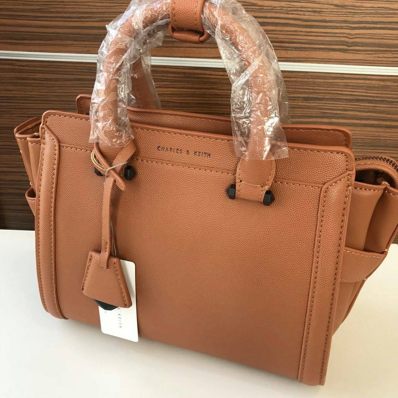 CHARLES & KEITH TRAPEZE BAG Best sellwr ! กระเป๋าถือหรือสะพายรุ่นยอดนิยมดีไซน์สวยหรูวัสดุหนัง คาเวียร์อยู่ทรง ด้านข้างเเต่งหนังช่องตัดดูมีดีเทล ด้านหน้าสกรีนโลโก้ ด้านหลังมีช่องซิป เปิดปิดด้วยซิปหัวซิป ปัํ๊มโลโก้ หูจับเเข็งแรง พับลงได้ พร้อมสายสะพายหนังปร