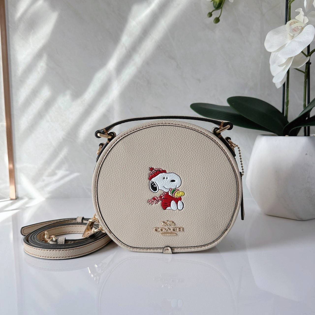 COACH X PEANUTS CANTEEN CROSSBODY WITH SNOOPY PRESENT MOTIF (CE845,CF290) กระเป๋าสะพายข้างทรงกลมไซส์มินิ มีหูจับ วัสหนังแท้ ด้านหน้าโดดเด่นด้วยรูปการ์ตูนSnoopy