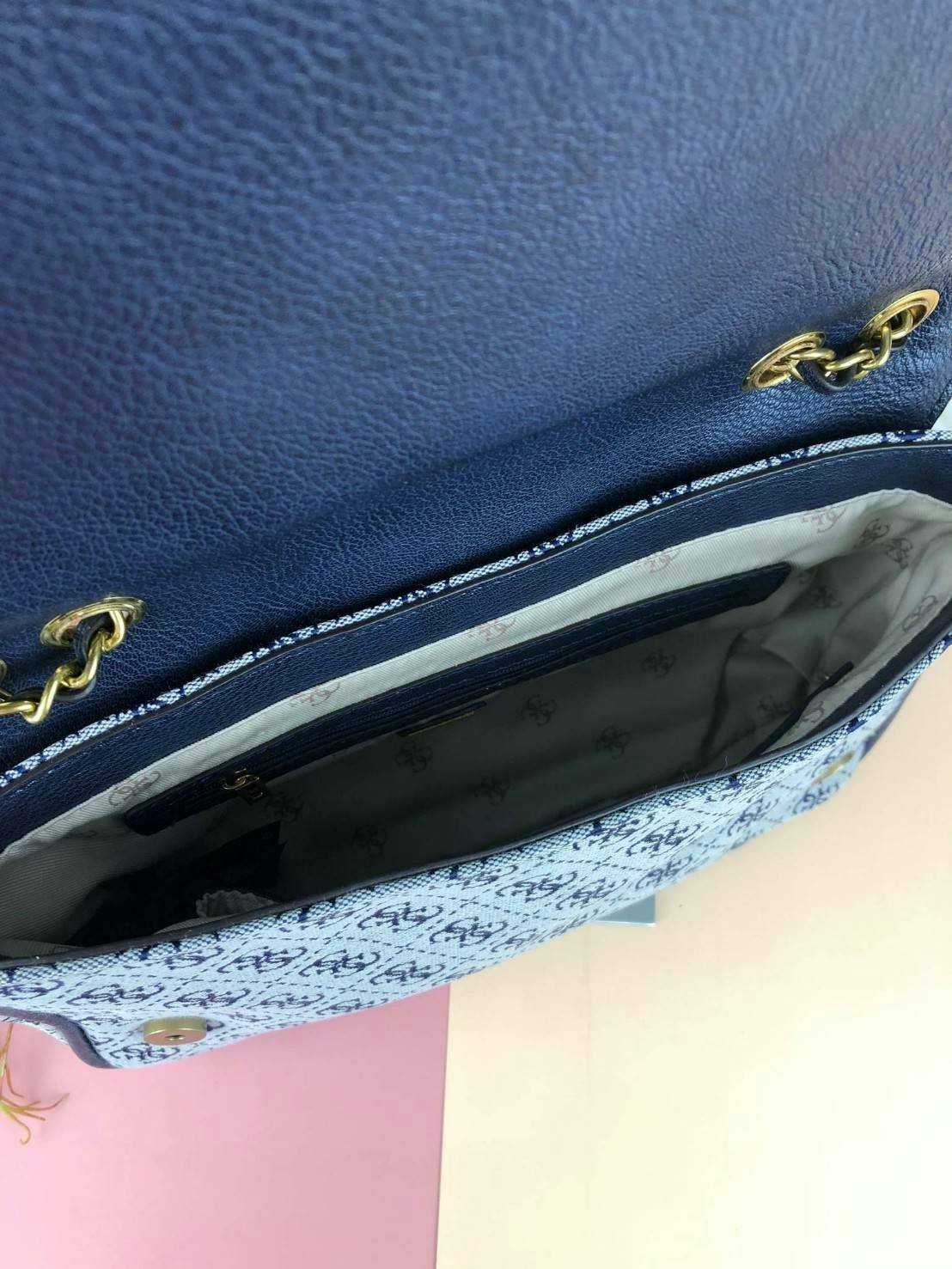 Guess Logo city handbag กระเป๋าสะพายไหล่ ตัวกระเป๋าเป็นผ้าลาย signature ของแบรนด์ ตัดกับหนังที่ตัวขอบกระเป๋า มาพร้อมพวงกุญแจโลโก้แบรนด์ ด้านหน้ามีโลโก้แบรนด์ ด้านหลังมีช่องใส่โทรศัพท์/บัตรได้ เปิดปิดแบบกระดุมแม่เหล็กซ้าย-ขวา ด้านในมีช่องซิป เล็ก 1 ช่อง แล