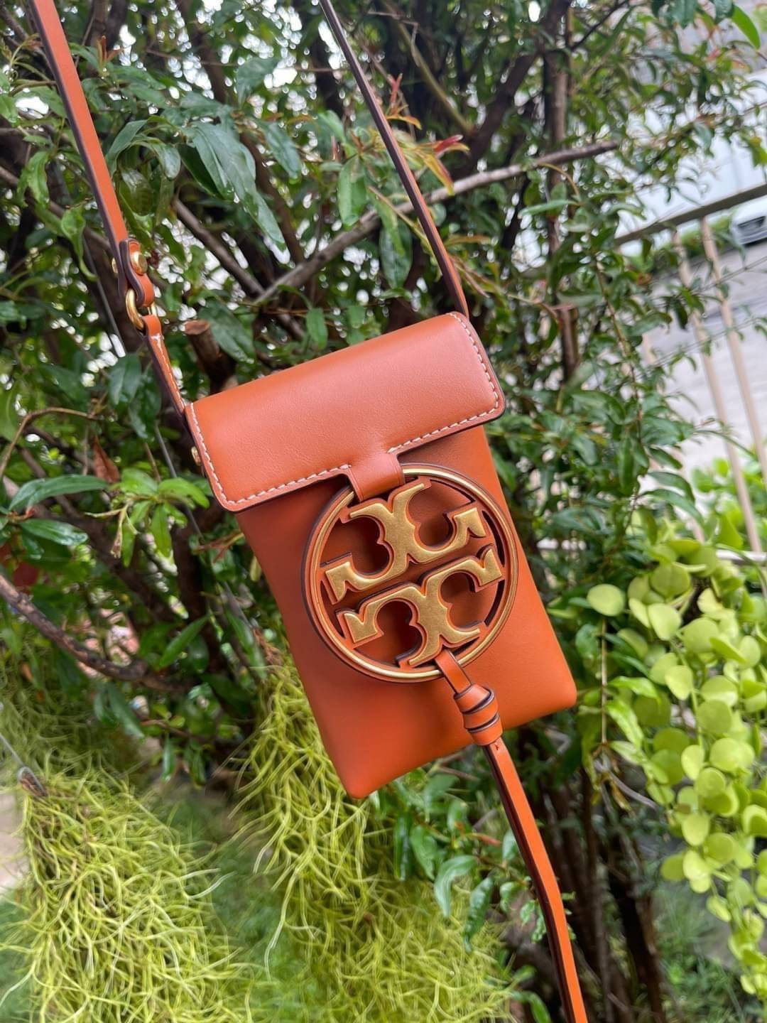 TORY BURCH MILLER METAL PHONE CROSSBODY อีกหนึ่งกระเป๋าใส่มือถือรุ่นฮิตที่เชื่อว่าหลาย ๆ คนต้องเคยเห็นผ่าน ๆ ตามาอย่างแน่นอน กับแบรนด์ Tory Burch ดีไซน์กระเป๋าทรงฝาพับแม่เหล็กใช้งานง่าย มาพร้อมดีเทล Logo แบรนด์โดดเด่นสีทองตัดกับหนังแกะสีดำ ดูหรูดูแพง! แต่