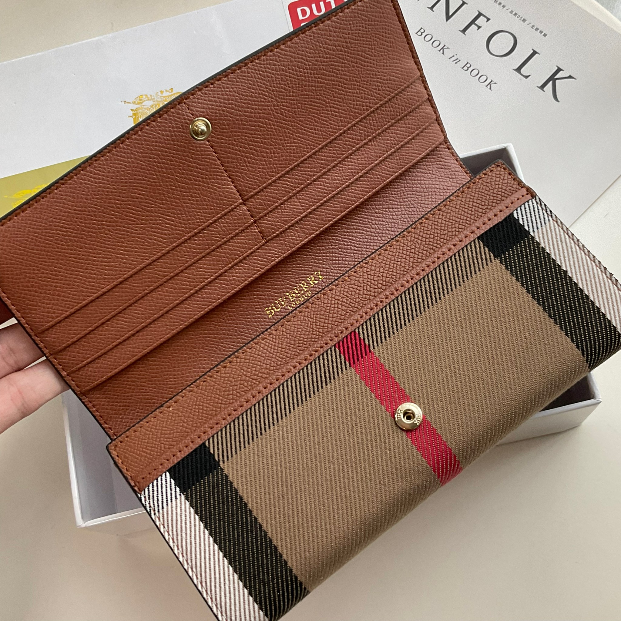 กระเป๋าสตางค์รับทรัพย์ ทรงหรู จากงาพรีเมี่ยมกิ๊ฟ Limited Edition จาก BURBERRY กระเป๋าสตางค์ใบยาวแบบพับกระดุม ทูโทนด้วยหนังแท้คาดผ้าลาย vintage ด้านในมีช่องใส่ธนบัตรยาวทั้งสองฝั่ง ช่องใส่บัตรได้อย่างน้อย 12 ช่อง และช่องเปิดด้วยซิปปั้มแบรนด์อะไหล่ทองสุดหรู 