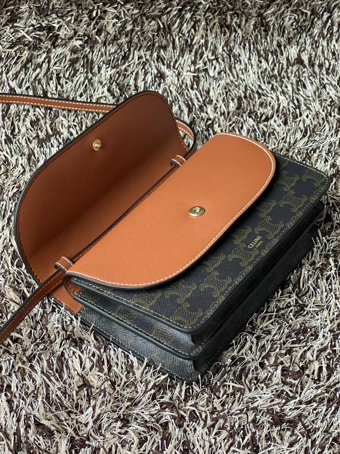 CELINE WALLET ON STRAP IN TRIOMPHE CANVAS กระเป๋าสะพายไหล่สุดเก๋ใบนี้ผลิตจากผ้าใบเคลือบอย่างดีพร้อมขอบหนังสีน้ำตาล กระเป๋ามีสายสะพายหนังสีน้ำตาลพร้อมฮาร์ดแวร์สีทอง ถอดสายออกเพื่อเป็นกระเป๋าถือทรงคลัชท์เปลี่ยนลุคช์ ลวดลายtriomphe ความเป็นแบรนด์ CELINE ได้อ