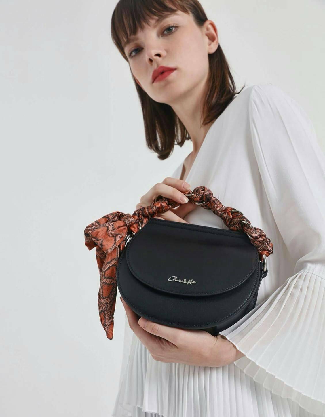 CHARLES & KEITH รุ่น LEATHER SATIN SCARF CROSSBODY BAG SL2-50150828 ราคาปกติช้อป ( ฿3,590.00 ) กระเป๋าถือ และ สะพาย ทรงโค้งมน หนังเรียบ ตั้งอยู่ทรง ด้านหน้าติดโลโก้แบรนด์ อะไหล่เงิน หูจับสายกระเป๋าร้อยเข้ากับห่วงเหล็กกลมๆ ด้วยผ้าลายสวยงามผูกเป็นโบว์เก๋ๆ ถ