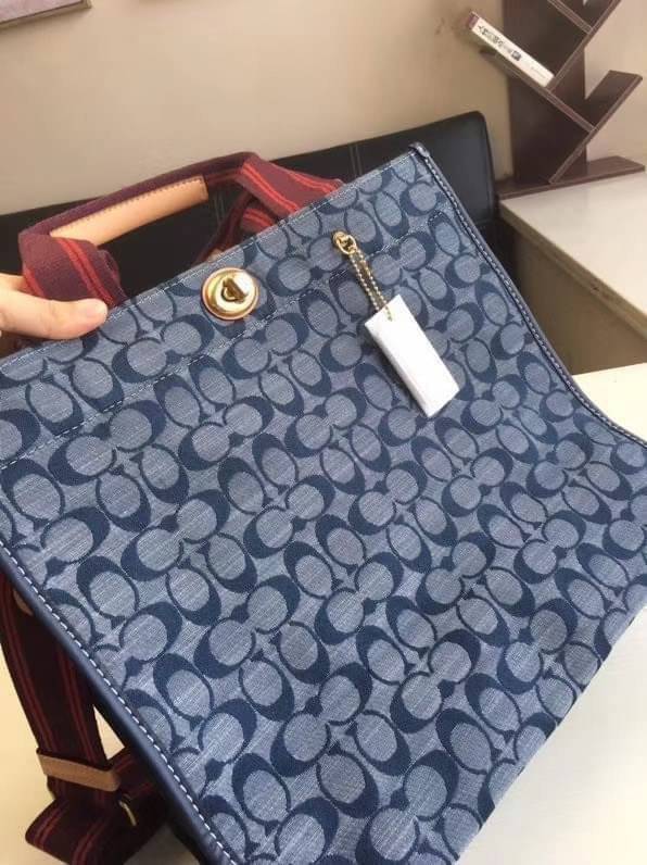 COACH Tote 34 In Signature Chambray หากคุณกำลังมองหากระเป๋าที่มีดีไซน์แปลกตา ไม่ค่อยเหมือนที่พบเห็นทั่วไป ต้องเป็นรุ่นนี้เลยค่ะ นอกจากจะผลิตจากผ้าแชมเบรย์ซึ่งมีน้ำหนักเบาแล้ว ยังให้สีสันคล้ายกับสียีนส์ สายสะพายและหูหิ้วสไตล์สปอร์ต ที่สำคัญยังมีหมุดปิดกระเ