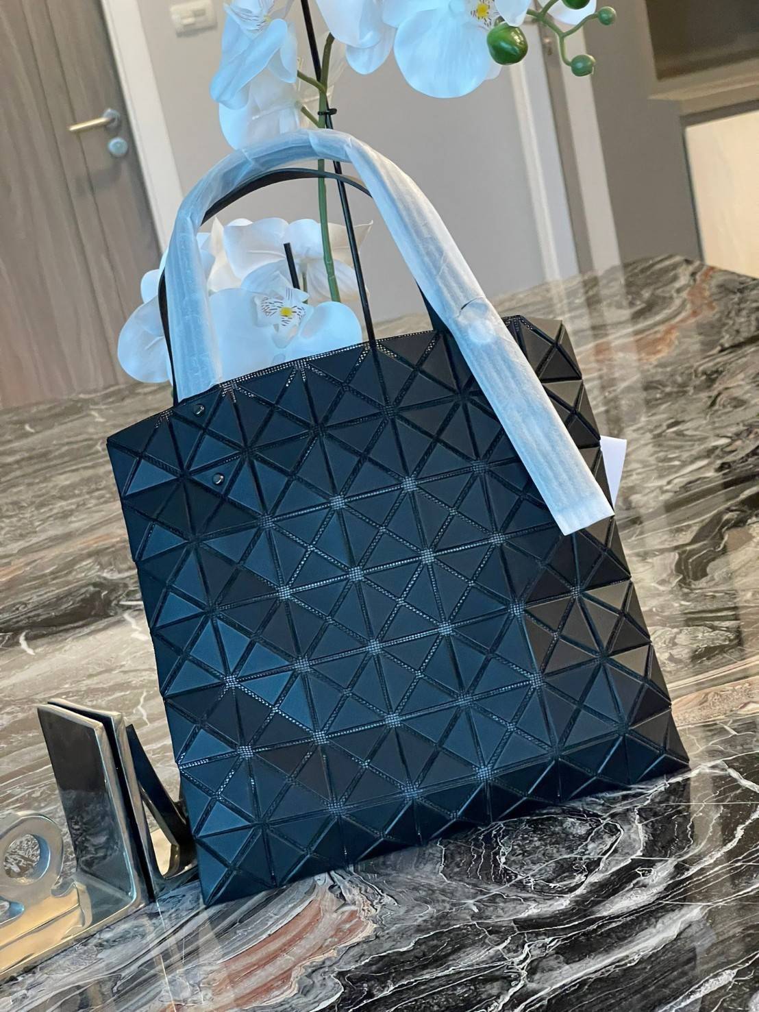 Baobao Issey Miyake Prism Kangaroo tote bag กระเป๋าถือทรงโท้ทที่ประดิษฐ์ขึ้นอย่างเชี่ยวชาญในญี่ปุ่น มาพร้อมแผงเรขาคณิตสำหรับการออกแบบที่ได้รับแรงบันดาลใจจากกระดาษพับ ซิลลูเอทอันเป็นเอกลักษณ์นี้ปิดท้ายด้วยสายรัดแบบอสมมาตร มีการพัฒนาโครงสร้างทรงสามเหลี่ยมเพ