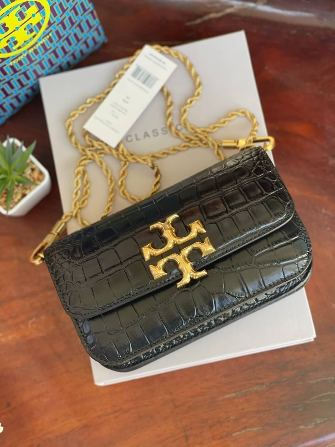 Tory Burch Eleanor Crocodile-Embossed Phone Crossbody Bag จุดเด่นของรุ่นนี้คือดีไซน์ออกมาในสไตล์คลาสสิกที่มาพร้อมกับฮาร์ดแวร์ที่ทำจากวัสดุทองเหลืองและสายสะพายโซ่เกลียวสีทอง ซึ่งการออกแบบได้รับแรงบันดาลใจมาจากเครื่องประดับ รูปทรงกะทัดรัดจึงสามารถสะพายใช้งา