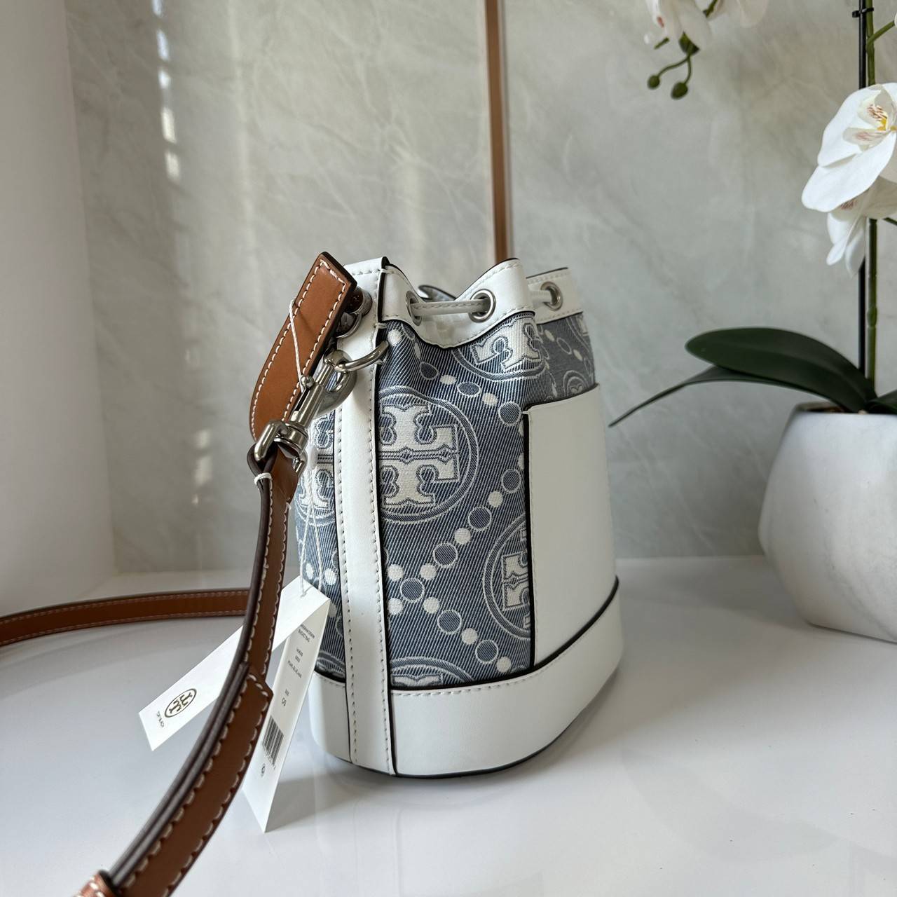 TORY BURCH T Monogram Denim Bucket Bag MEDIUM คอลเลคชั่นใหม่ รูปแบบคลาสสิค พกพาความหรูหราไปได้ทุกที่ด้วยกระเป๋าทรง Bucket ขนาดกลางและปิดด้วยเชือกรูดพร้อมโลโก้แวววาว วัสดุผ้าเดนิมแจ็คการ์ด ตัดขอบหนังแท้