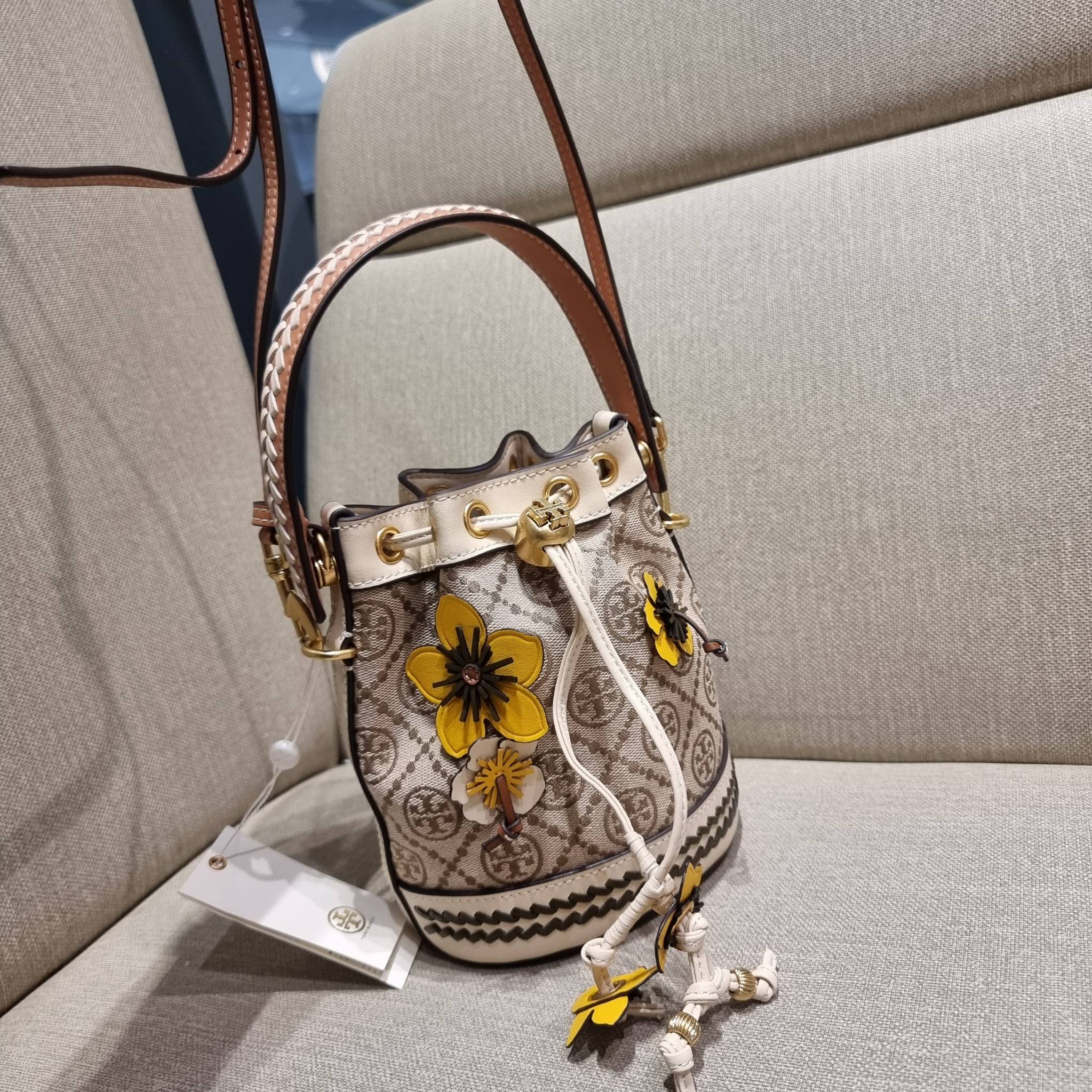 TORY BURCH MINI T MONOGRAM FLORAL BUCKET BAG คอลเลคชั่นใหม่ พร้อมเสิร์ฟความสวยให้ถึงบ้าน!! กระเป๋าบัคเก็ตทรงยอดนิยม ไซส์มินิ ดีไซน์ใหม่ล่าสุด สไตล์งานคราฟ มีลูกเล่นประดับดอกไม้กับตัวกระเป๋า และตัวรูดสาย วัสดุผ้า jacquard ตัดสลับหนังแท้ หูจับและขอบกระเป๋าต