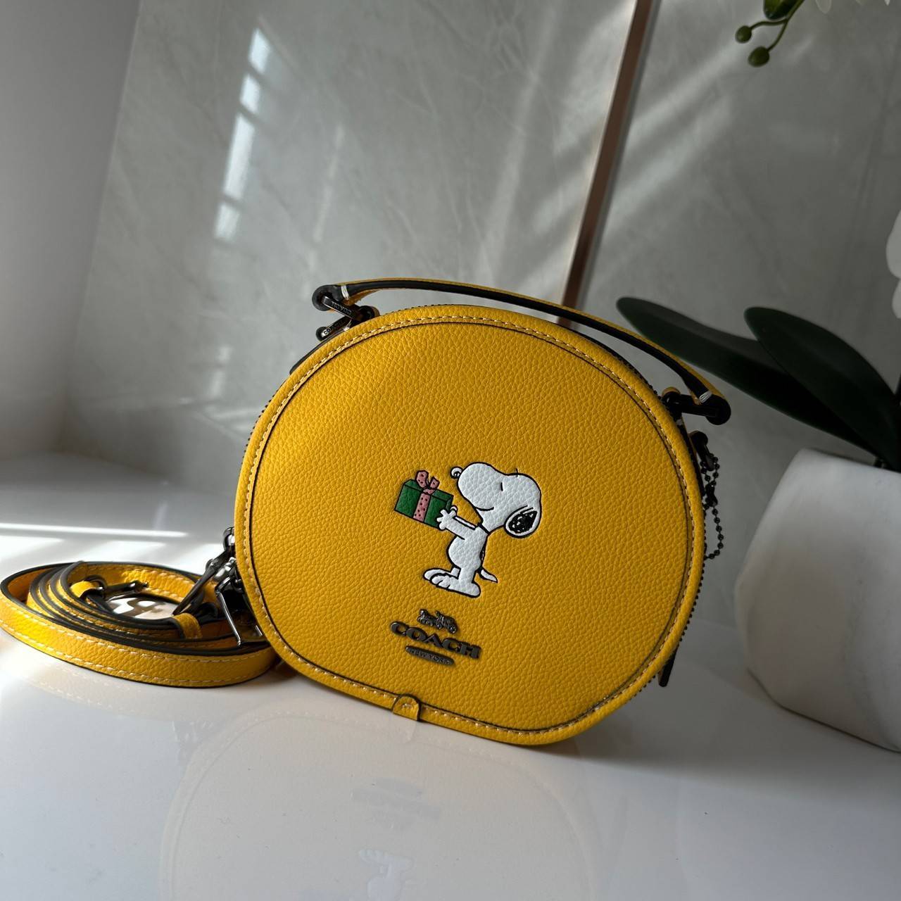 COACH X PEANUTS CANTEEN CROSSBODY WITH SNOOPY PRESENT MOTIF (CE845,CF290) กระเป๋าสะพายข้างทรงกลมไซส์มินิ มีหูจับ วัสหนังแท้ ด้านหน้าโดดเด่นด้วยรูปการ์ตูนSnoopy