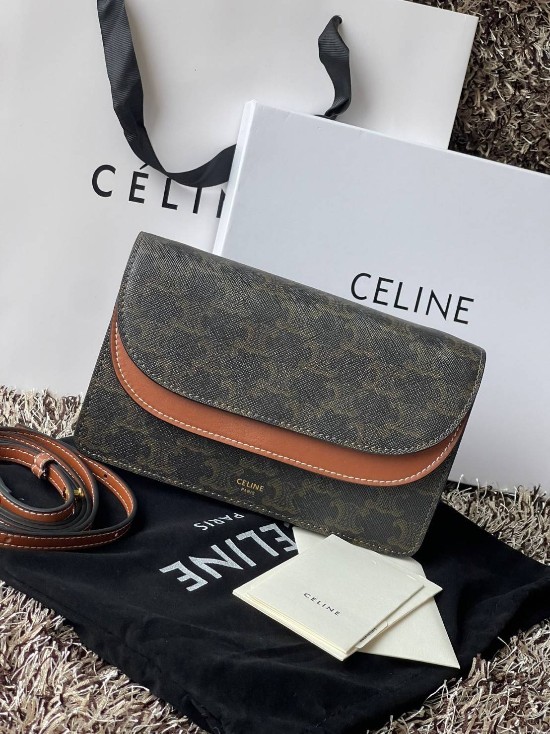 CELINE WALLET ON STRAP IN TRIOMPHE CANVAS กระเป๋าสะพายไหล่สุดเก๋ใบนี้ผลิตจากผ้าใบเคลือบอย่างดีพร้อมขอบหนังสีน้ำตาล กระเป๋ามีสายสะพายหนังสีน้ำตาลพร้อมฮาร์ดแวร์สีทอง ถอดสายออกเพื่อเป็นกระเป๋าถือทรงคลัชท์เปลี่ยนลุคช์ ลวดลายtriomphe ความเป็นแบรนด์ CELINE ได้อ
