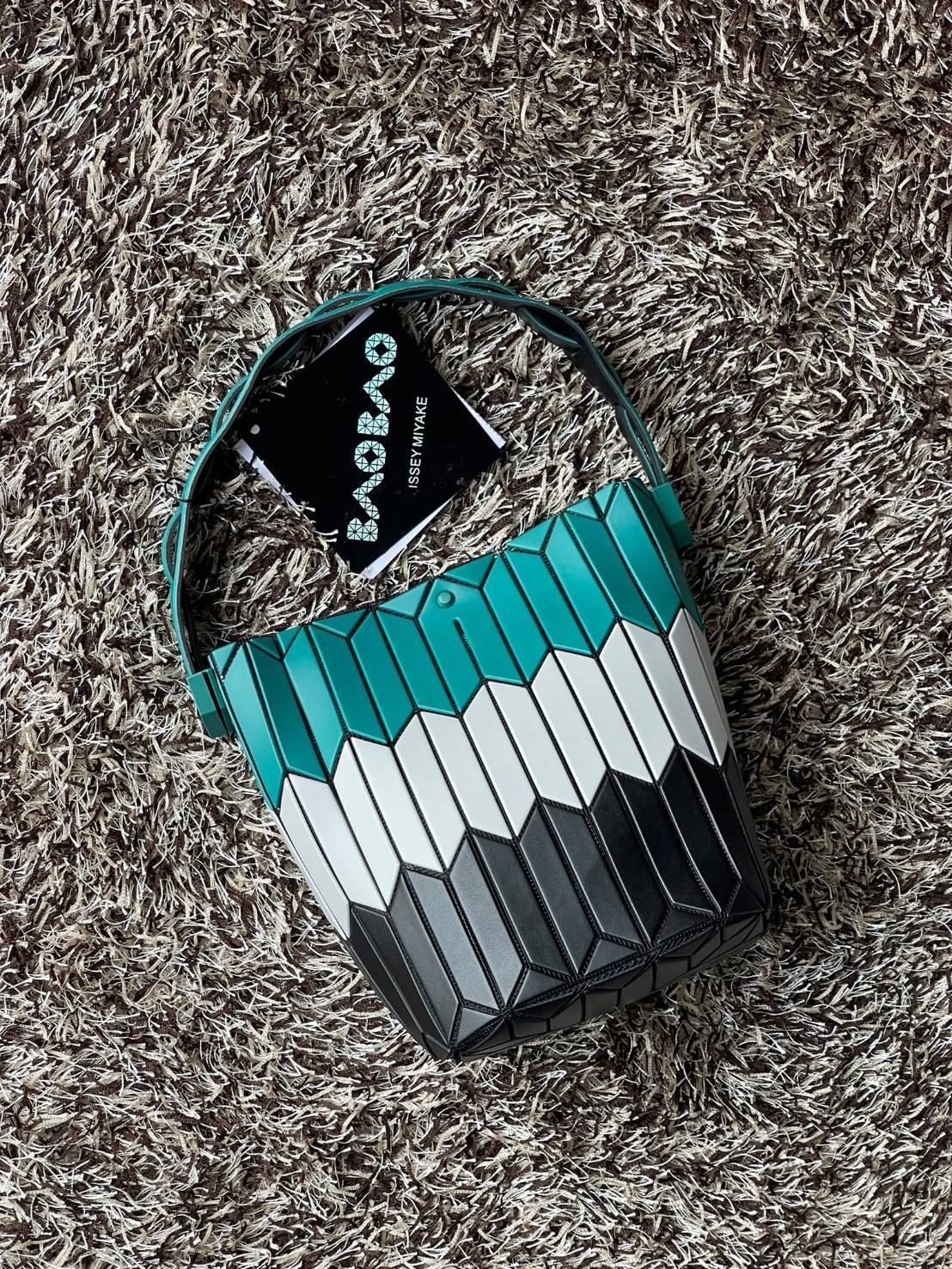 Small : BAO BAO ISSEY MIYAKE SMALL BUCKET เป็นกระเป๋าบัคเก็ตขนาดเล็กสามารถใช้ใส่กระเป๋าสตางค์และโทรศัพท์มือถือได้ ซีรีย์ใหม่นี้มีจุดเด่นที่แผ่นรูปทรงสี่เหลี่ยมด้านขนานในแนวตั้ง เกิดเป็นรูปทรงสามมิติซึ่งแตกต่างไปจากรูปทรงที่เกิดขึ้นจากแผ่นสามเหลี่ยม หูหิ้ว