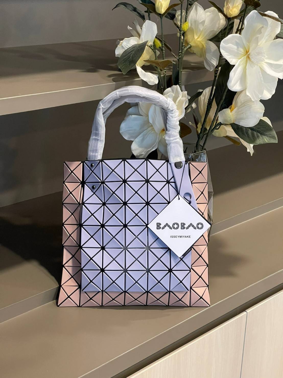 Baobao Issey Miyake Prism Kangaroo tote bag กระเป๋าถือทรงโท้ทที่ประดิษฐ์ขึ้นอย่างเชี่ยวชาญในญี่ปุ่น มาพร้อมแผงเรขาคณิตสำหรับการออกแบบที่ได้รับแรงบันดาลใจจากกระดาษพับ ซิลลูเอทอันเป็นเอกลักษณ์นี้ปิดท้ายด้วยสายรัดแบบอสมมาตร มีการพัฒนาโครงสร้างทรงสามเหลี่ยมเพ