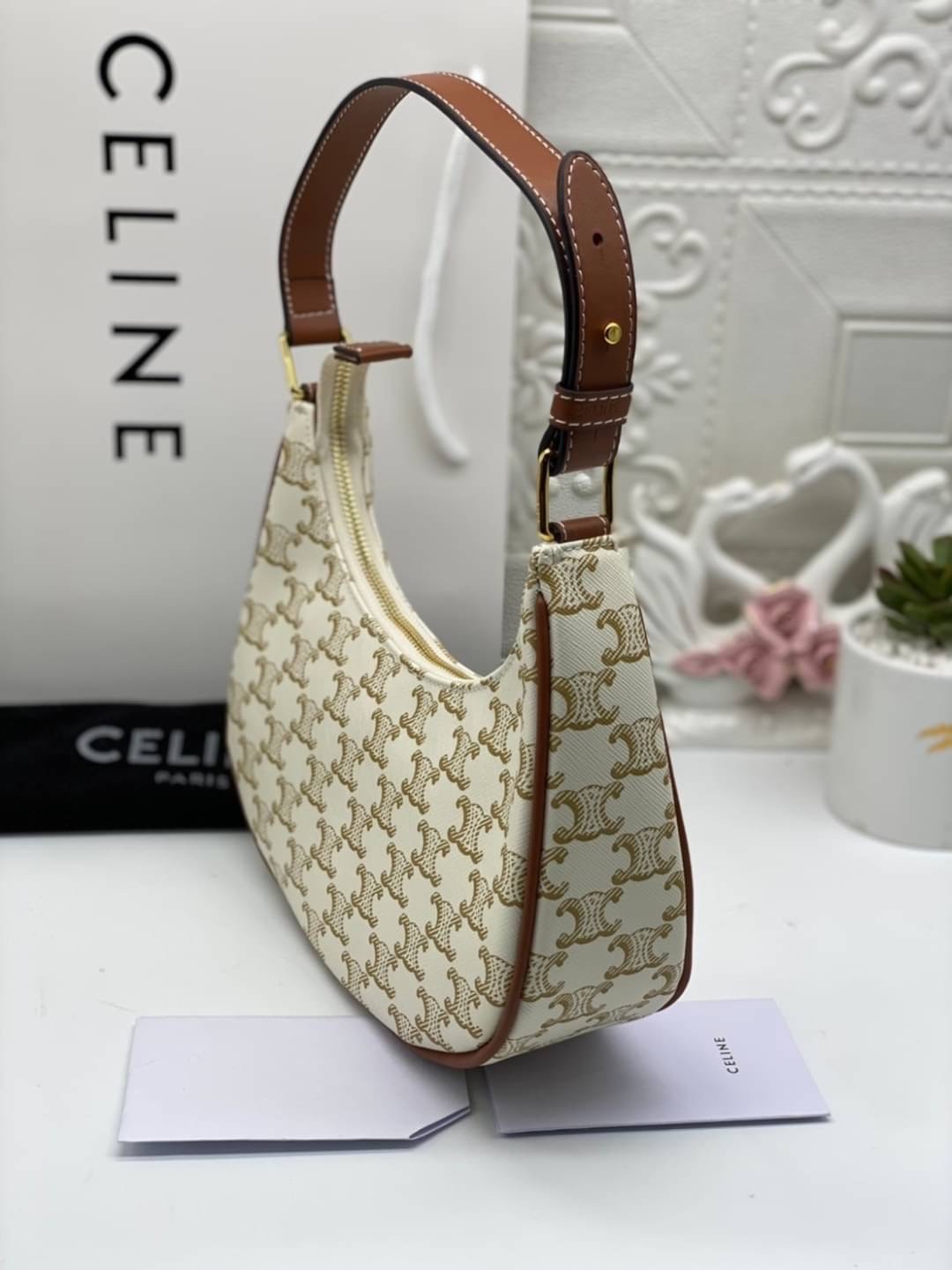หนังแท้ CELINE AVA / CELINE Vintage Classic Ava bag 1 ใน คอลเลคชั่น “Triomphe Canvas” มาพร้อมสายสะพายไหล่ที่ปรับความยาวได้ และเนื่องจากช่วงล่างของกระเป๋ามีขนาดใหญ่กว่าช่วงบน จึงทำให้ไม่เสียทรงเมื่อเราใส่สิ่งของอย่างกระเป๋าสตางค์หรือโทรศัพท์มือถือ หากดูภาพ