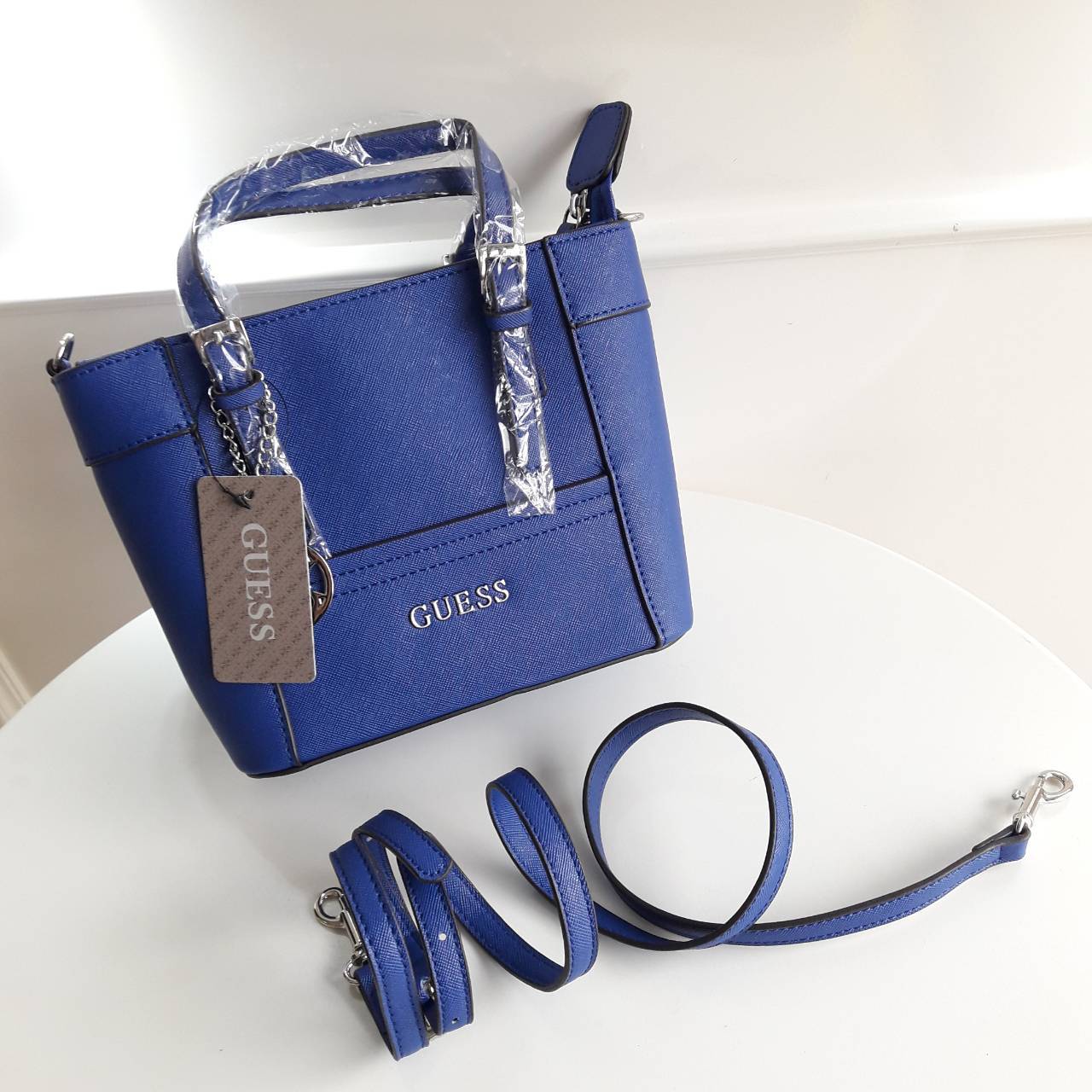 New! guess mini tote saffiano bag ลายหนัง Saffiano สวยอยู่ทรงสไตล์ PRADA ขนาดกำลังดีน้ำหนักเบา ด้านหน้าประดับโลโก้แบร์น พร้อมพวงกุญแจโลโก้แบรนด์ห้อยที่หูกระเป๋าสามารถถอดเเยกใช้ได้ เปิดปิดด้วยซิปสะดวกใช้ ภายในมีโลโก้ ช่องซิปและช่องเล็กใส่มือถือ ซับในพิมโลโ