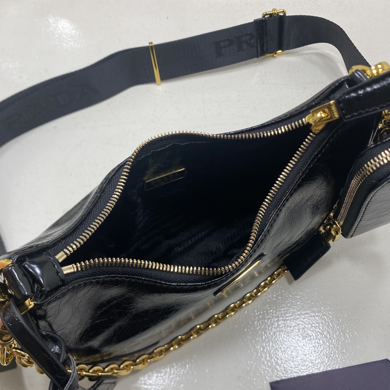 ORI หนังแท้ | Prada Re-Edition 2005 bag in Naplak leather กระเป๋าสะพายทรงโฮโบหนังแก้ว ดีไซน์เอฟเฟกต์มันวาวและเท็กซ์เจอร์ที่มีเสน่ห์สไตล์วินเทจ พร้อมทริกห้อยเพิ่มสไตล์สัมผัสที่โดดเด่นและร่วมสมัยยิ่งขึ้น