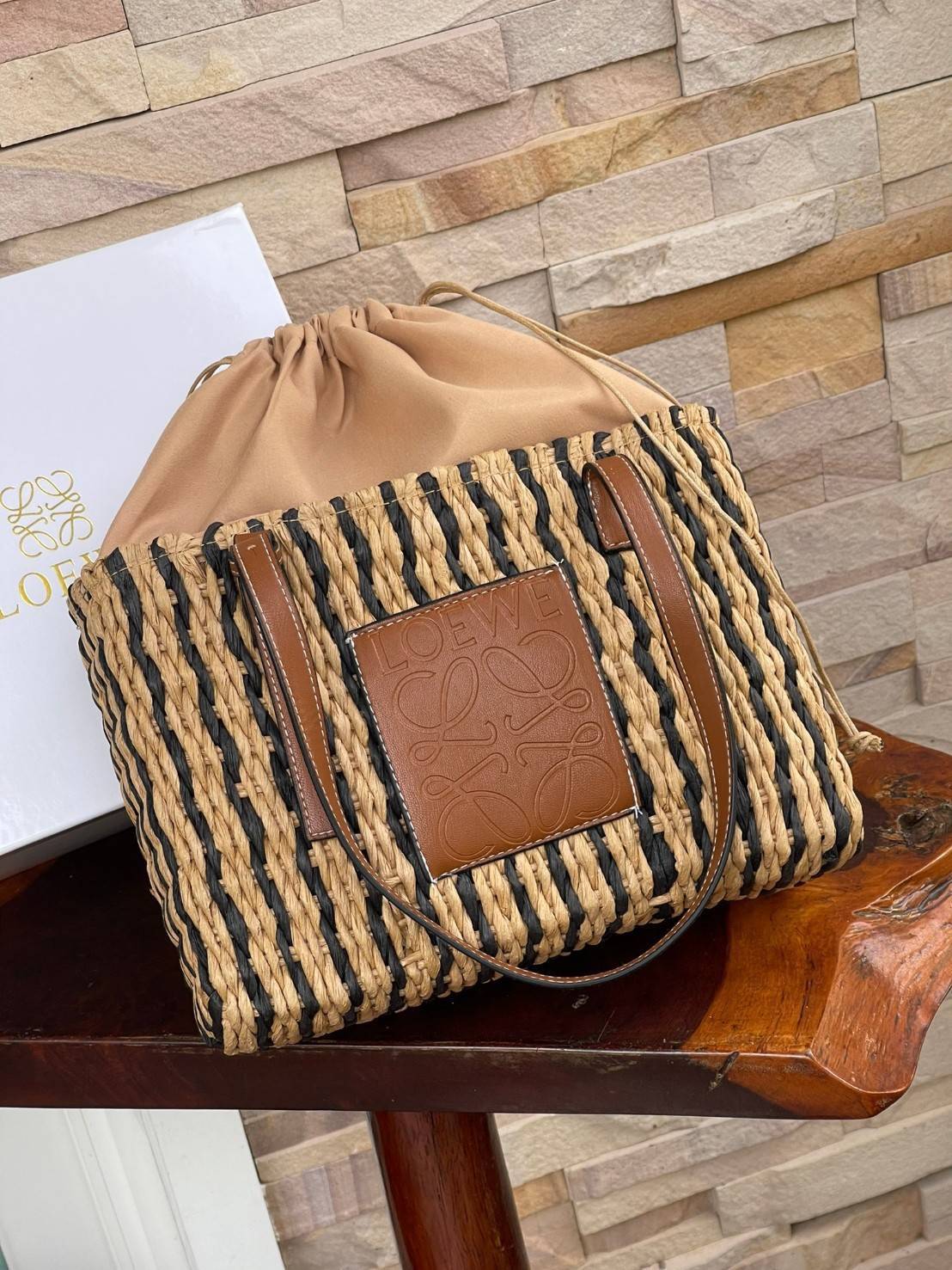 LOEWE X PAULA'S IBIZA SMALL SQUARE BASKET BAG กระเป๋าสะพายไหล่จากโลเอเว่ เป็นกระเป๋าสานขึ้นจากใบกก (Reed) ที่มีทั้งความเหนียวและความยืดหยุ่น สวยน่ารักแบบมินิมอล มีความทนทานสูง ดูแลรักษาง่าย ด้านหน้าและหูเป็นหนังแท้(calf skin) ส่วนภายในมีถุงผ้าแบบหูรู