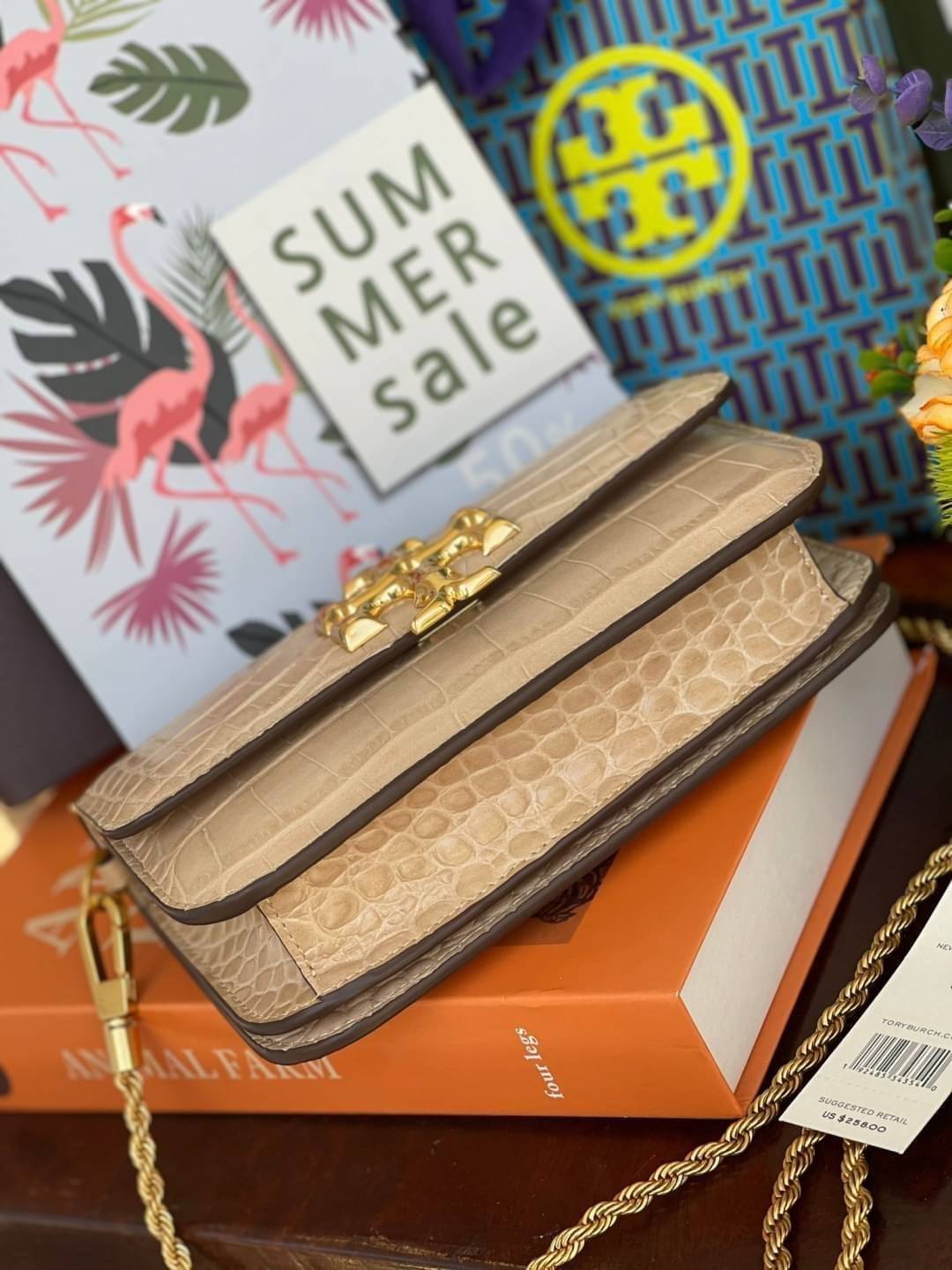 Tory Burch Eleanor Crocodile-Embossed Phone Crossbody Bag จุดเด่นของรุ่นนี้คือดีไซน์ออกมาในสไตล์คลาสสิกที่มาพร้อมกับฮาร์ดแวร์ที่ทำจากวัสดุทองเหลืองและสายสะพายโซ่เกลียวสีทอง ซึ่งการออกแบบได้รับแรงบันดาลใจมาจากเครื่องประดับ รูปทรงกะทัดรัดจึงสามารถสะพายใช้งา