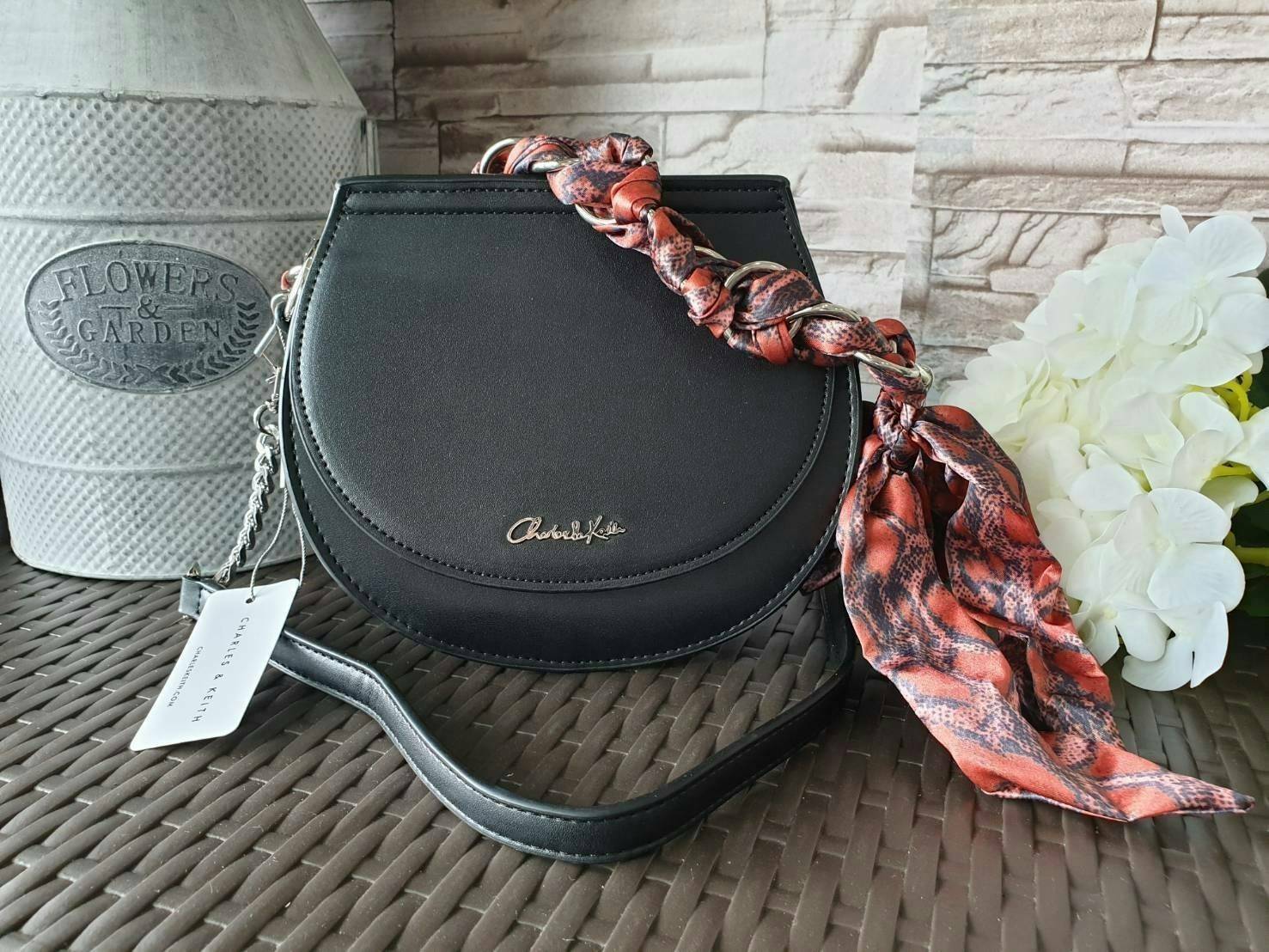 CHARLES & KEITH รุ่น LEATHER SATIN SCARF CROSSBODY BAG SL2-50150828 ราคาปกติช้อป ( ฿3,590.00 ) กระเป๋าถือ และ สะพาย ทรงโค้งมน หนังเรียบ ตั้งอยู่ทรง ด้านหน้าติดโลโก้แบรนด์ อะไหล่เงิน หูจับสายกระเป๋าร้อยเข้ากับห่วงเหล็กกลมๆ ด้วยผ้าลายสวยงามผูกเป็นโบว์เก๋ๆ ถ