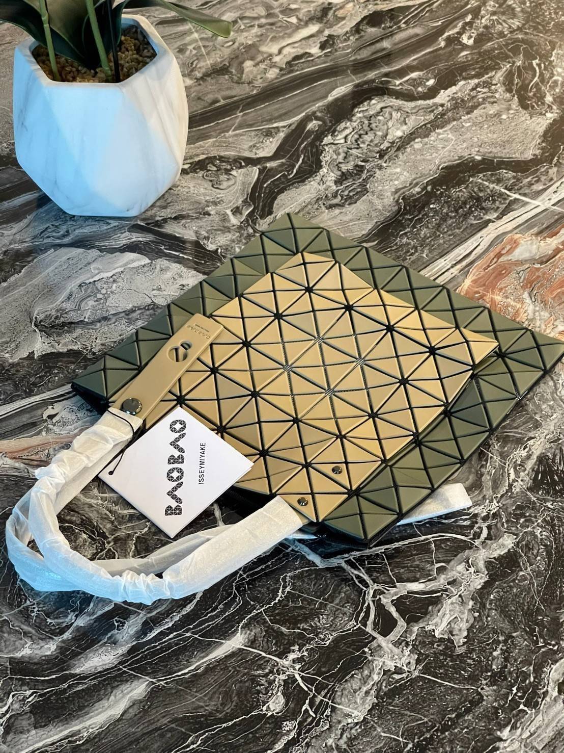 Baobao Issey Miyake Prism Kangaroo tote bag กระเป๋าถือทรงโท้ทที่ประดิษฐ์ขึ้นอย่างเชี่ยวชาญในญี่ปุ่น มาพร้อมแผงเรขาคณิตสำหรับการออกแบบที่ได้รับแรงบันดาลใจจากกระดาษพับ ซิลลูเอทอันเป็นเอกลักษณ์นี้ปิดท้ายด้วยสายรัดแบบอสมมาตร มีการพัฒนาโครงสร้างทรงสามเหลี่ยมเพ