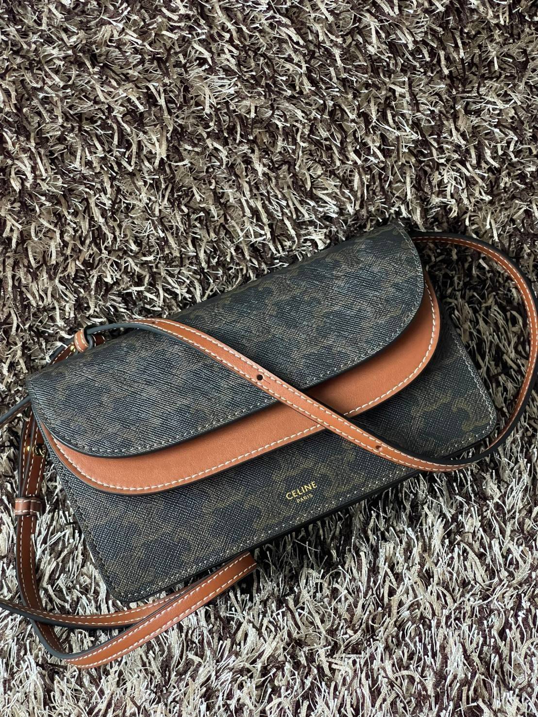 CELINE WALLET ON STRAP IN TRIOMPHE CANVAS กระเป๋าสะพายไหล่สุดเก๋ใบนี้ผลิตจากผ้าใบเคลือบอย่างดีพร้อมขอบหนังสีน้ำตาล กระเป๋ามีสายสะพายหนังสีน้ำตาลพร้อมฮาร์ดแวร์สีทอง ถอดสายออกเพื่อเป็นกระเป๋าถือทรงคลัชท์เปลี่ยนลุคช์ ลวดลายtriomphe ความเป็นแบรนด์ CELINE ได้อ