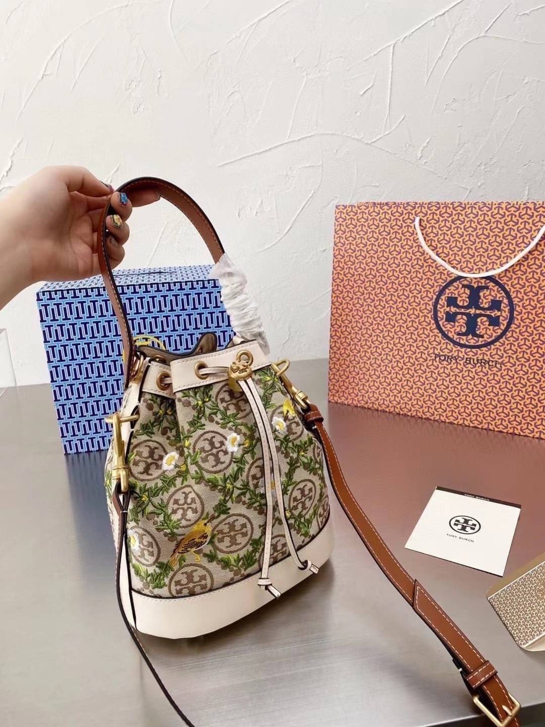 TORY BURCH T MONOGRAM JACQUARD EMBROIDERED BUCKET BAG ครั้งแรกกับโมโนแกรม ที่ได้รับแรงบันดาลใจมาจากโลโก้สุดคลาสสิก กลับมาอีกครั้งในรูปแบบของ ลวดลาย T Monogram ที่ผสมผสานความร่วมสมัยเข้ากับความเป็นเอกลักษณ์ของแบรนด์เข้าไว้ด้วยกัน โดยเป็นการนำเอาลวดลาย T Mo