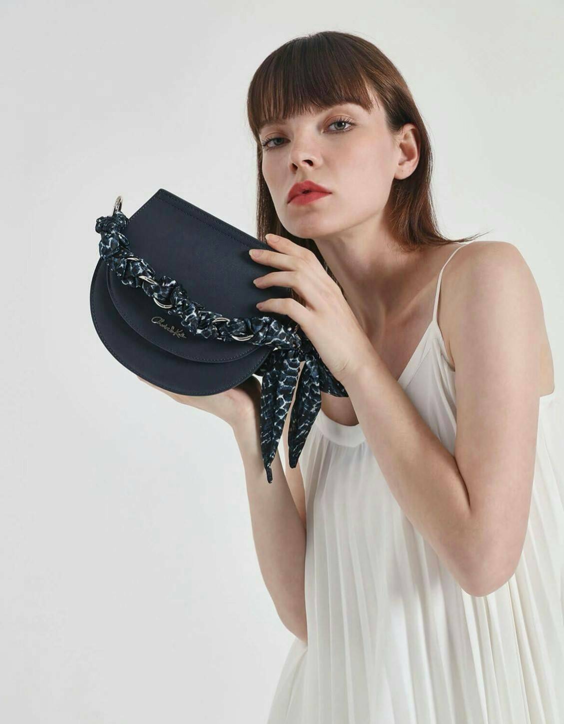 CHARLES & KEITH รุ่น LEATHER SATIN SCARF CROSSBODY BAG SL2-50150828 ราคาปกติช้อป ( ฿3,590.00 ) กระเป๋าถือ และ สะพาย ทรงโค้งมน หนังเรียบ ตั้งอยู่ทรง ด้านหน้าติดโลโก้แบรนด์ อะไหล่เงิน หูจับสายกระเป๋าร้อยเข้ากับห่วงเหล็กกลมๆ ด้วยผ้าลายสวยงามผูกเป็นโบว์เก๋ๆ ถ