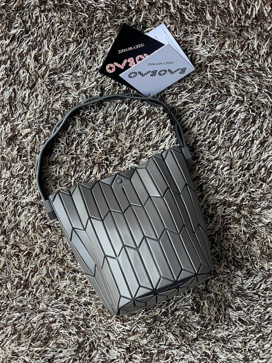 Small : BAO BAO ISSEY MIYAKE SMALL BUCKET เป็นกระเป๋าบัคเก็ตขนาดเล็กสามารถใช้ใส่กระเป๋าสตางค์และโทรศัพท์มือถือได้ ซีรีย์ใหม่นี้มีจุดเด่นที่แผ่นรูปทรงสี่เหลี่ยมด้านขนานในแนวตั้ง เกิดเป็นรูปทรงสามมิติซึ่งแตกต่างไปจากรูปทรงที่เกิดขึ้นจากแผ่นสามเหลี่ยม หูหิ้ว