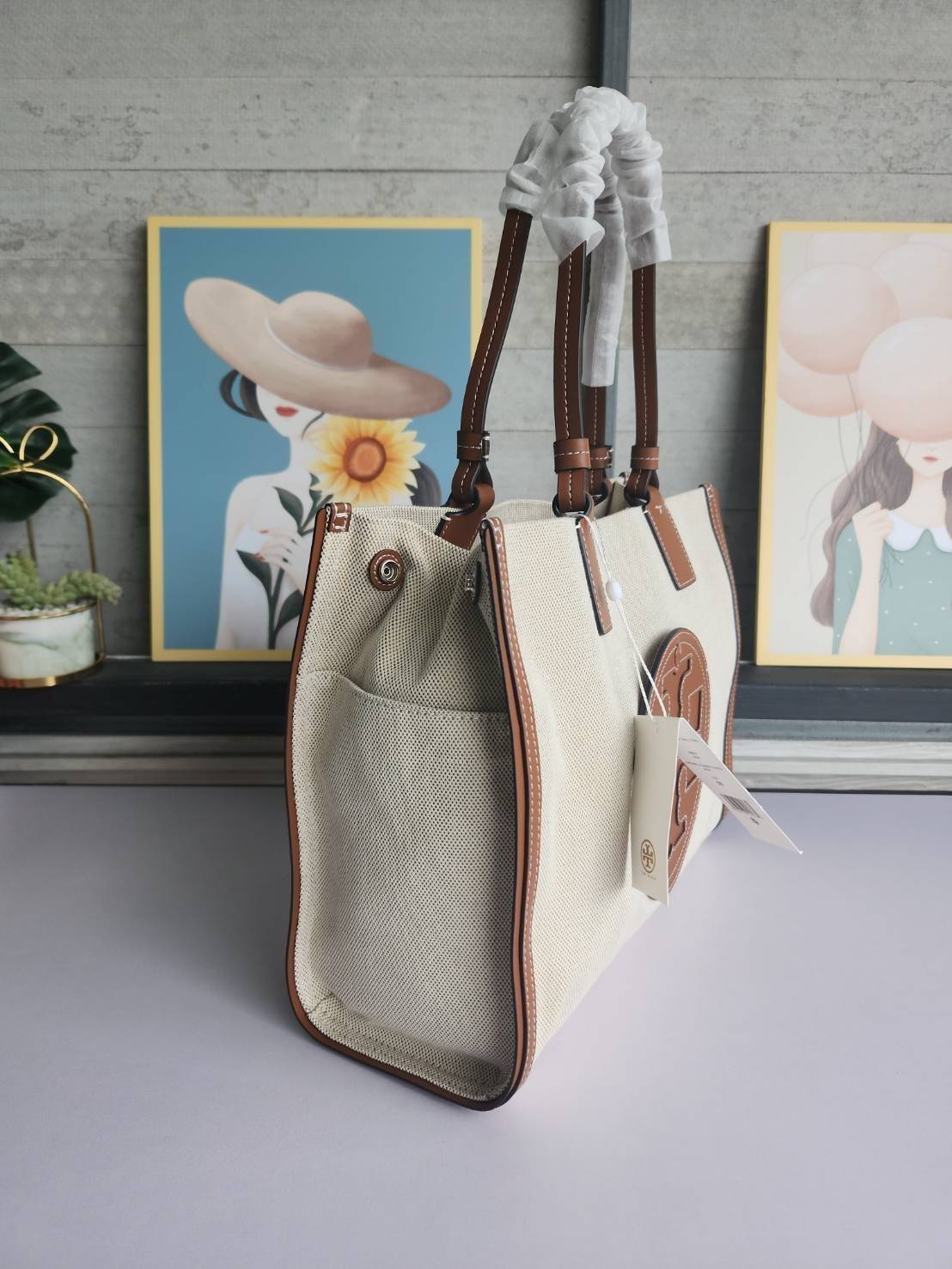 TORY BURCH ELLA CANVAS TOTE BAG กระเป๋าโท้ตน้ำหนักเบาของเราพร้อมป้ายโลโก้ Ella ทำจากผ้าใบที่ทนทานพร้อมรายละเอียดหนังและกระเป๋าด้านใน อเนกประสงค์ ทรงคลาสสิก และสร้างขึ้นอย่างสวยงามด้วยฝีมือช่างฝีมือ สายรัดแคบช่วยให้วางราบกับไหล่ได้อย่างสบาย เหมาะสำหรับทุกว