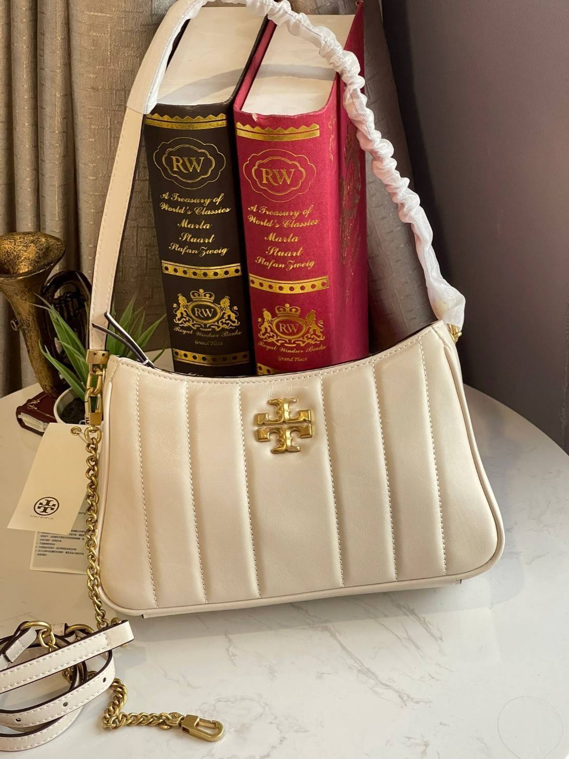Tory burch Kira logo-plaque crossbody bag กระเป๋า Kira ของ Tory Burch เป็นส่วนหนึ่งของคอลเล็กชั่นที่โดดเด่น และมีหลายรุ่นด้วยกัน โดยมีป้ายโลโก้ Double T ของแบรนด์อยู่ตรงกลาง มีความเรียบง่ายแต่ยังคงความหรูหราโดดเด่นด้วยวัสดุบุผิว ป้ายโลโก้สีทอง สายสะพายโซ่