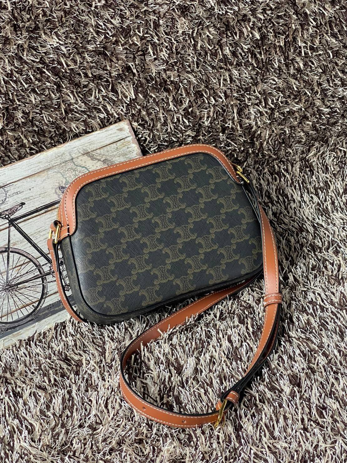 CELINE Triomphe Canvas Small Camera กระเป๋าสะพายไหล่สุดเก๋ใบนี้ผลิตจากผ้าใบเคลือบอย่างดีพร้อมขอบหนังสีน้ำตาล มาพร้อมสายสะพายหนังปรับระดับได้พร้อมฮาร์ดแวร์สีทองและซิปด้านบน ภายในบุด้วยผ้าสีน้ำตาล ลวดลาย triomphe อันเป็นเอกลักษณ์ของแบรนด์ และเป็นกระเป๋าสะพา