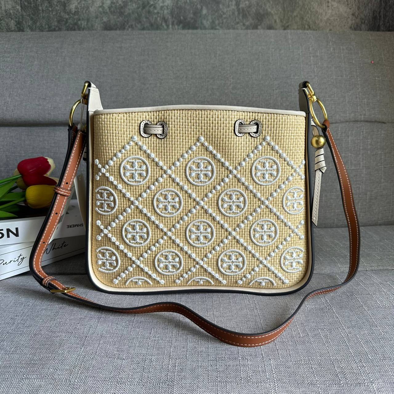 TORY BURCH T Monogram Straw Bell Bag กระเป๋าสะพายข้างรุ่นคลาสสิกที่ได้แรงบันดาลใจจากการควิลท์แบบดั้งเดิมของเพนซิลเวเนีย คอลเลกชันบ่งบอกถึงความมีสไตล์เหนือกาลเวลา รูปทรงเรียวโดดเด่น ปักทอลายแบรนด์อย่างสวยงาม เปิด ปิดด้วยเชือกรูด ด้านในช่องโล่งกว้าง ซับในผ้