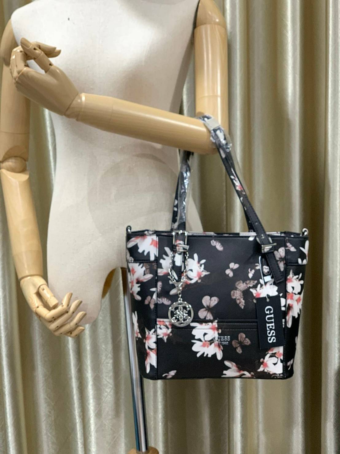 GUESS Women's Medium Floral Tote Bag กระเป๋าถือ คล้องไหล่หรือสะพาย ขนาดกลาง วัสดุหนังpu ลายดอกไม้ชนิดต่างๆรอบใบ เปิดปิดใช้งานด้วยซิปเดียวด้านบน ภายในมีกว้างใส่กระเป๋าสตาวค์ยาว มินิไอแพคได้ หูจับและสายสะพายปรับระดับได้ มาพร้อมกุญแจโลโก้guess สวยน่ารัก