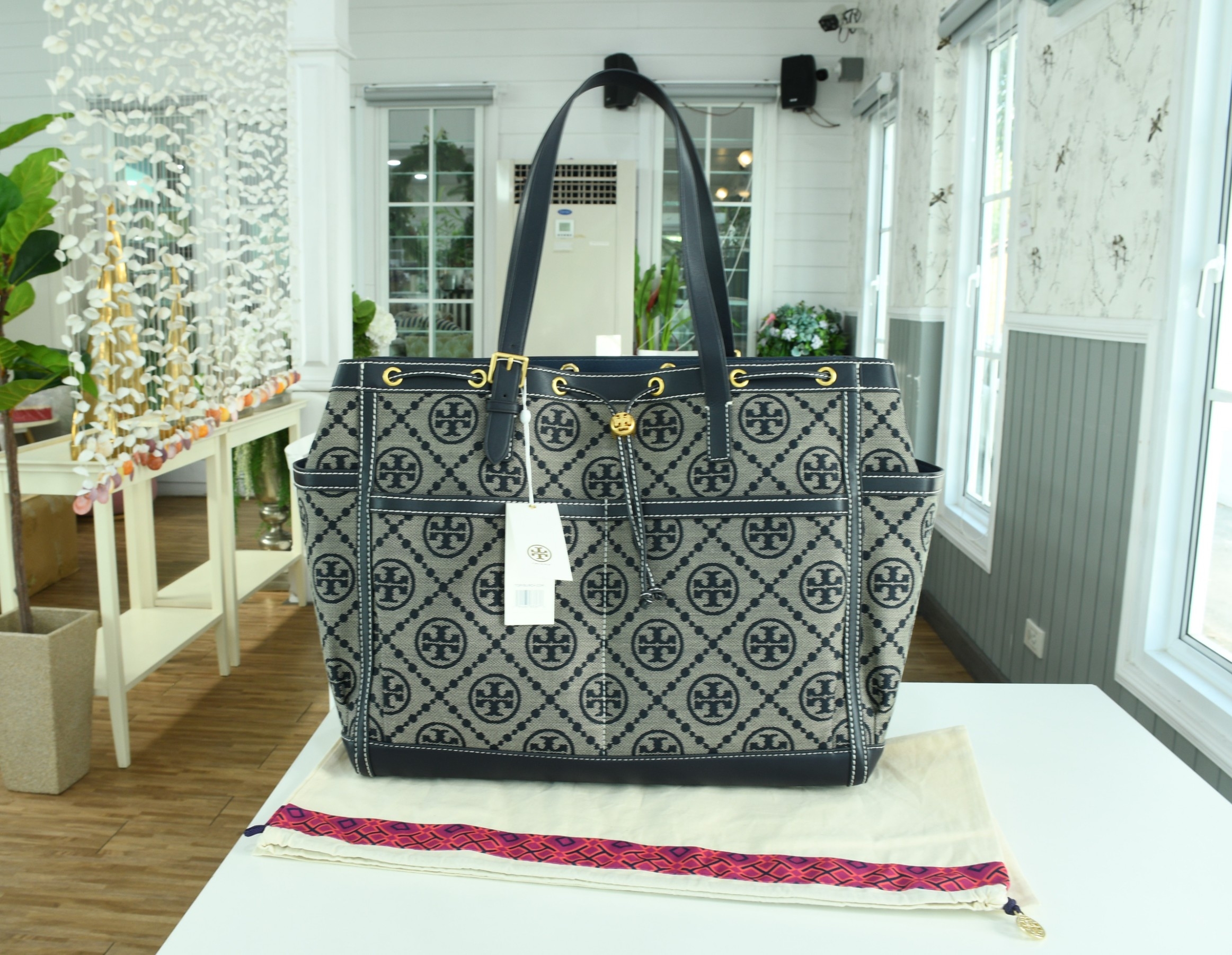 OUTLET 】TORY T MONOGRAM JACQUARD WFH TOTE กระเป๋าถือหรือสะพายไหล่ วัสดุ Canvas ปักษ์ลายแบรนด์ อะไหล่ทองสวยหรู น้ำหนักเบา จุของได้เยอะ ด้านหน้ามีกระเป๋าเล็ก2ช่อง ด้านหลัง2ช่อง ด้านในโล่ง มีช่องใหญ่1ช่อง ช่องเล็ก1ช่อง และอีก1ช่องซิป ใบใหญ่ Size XL ใส่เสื้อผ