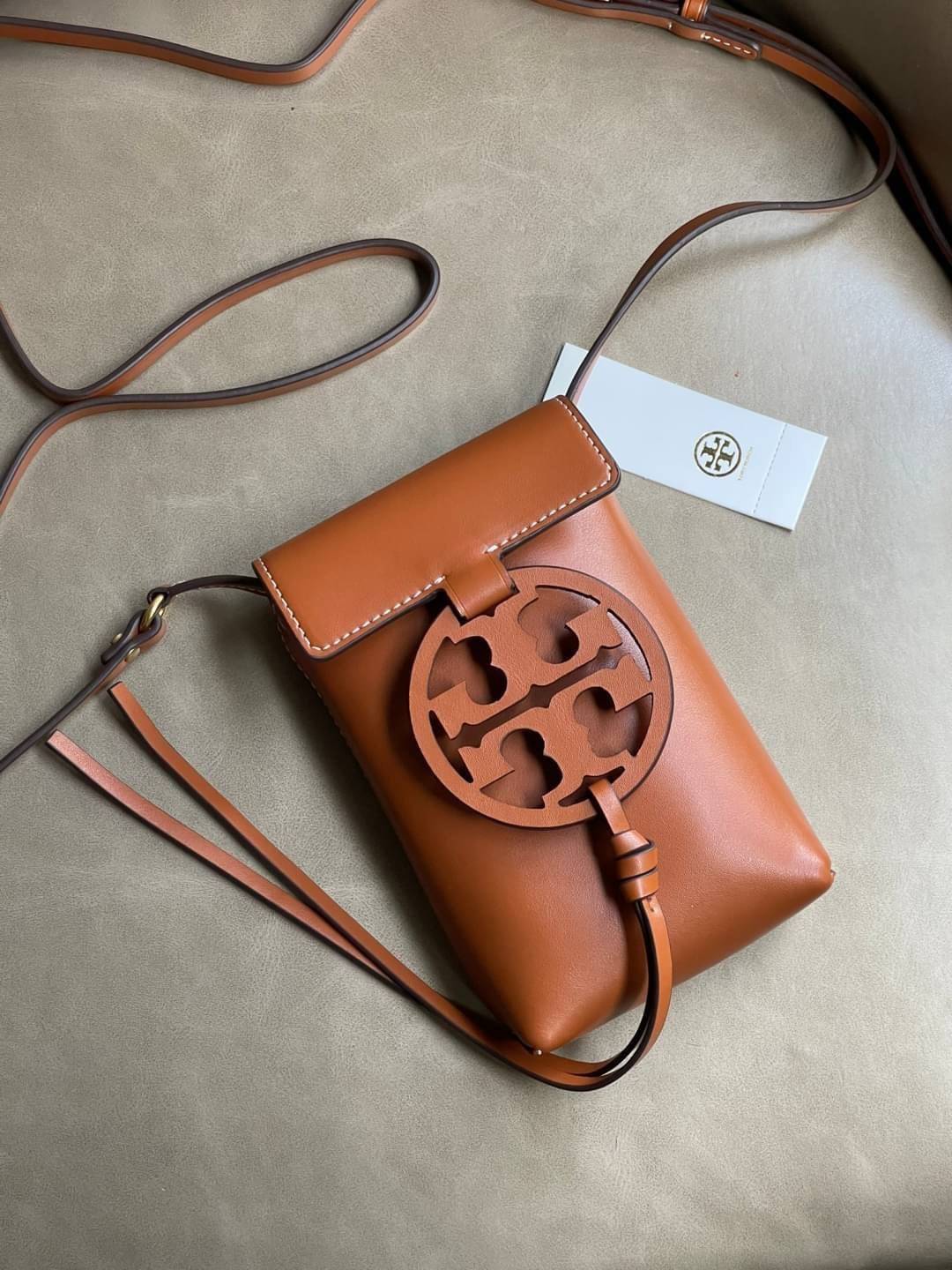 TORY BURCH MILLER METAL PHONE CROSSBODY อีกหนึ่งกระเป๋าใส่มือถือรุ่นฮิตที่เชื่อว่าหลาย ๆ คนต้องเคยเห็นผ่าน ๆ ตามาอย่างแน่นอน กับแบรนด์ Tory Burch ดีไซน์กระเป๋าทรงฝาพับแม่เหล็กใช้งานง่าย มาพร้อมดีเทล Logo สีเดียวกับเฉดสีของกระเป๋า แต่ยังมีความน่ารักด้วยทรง