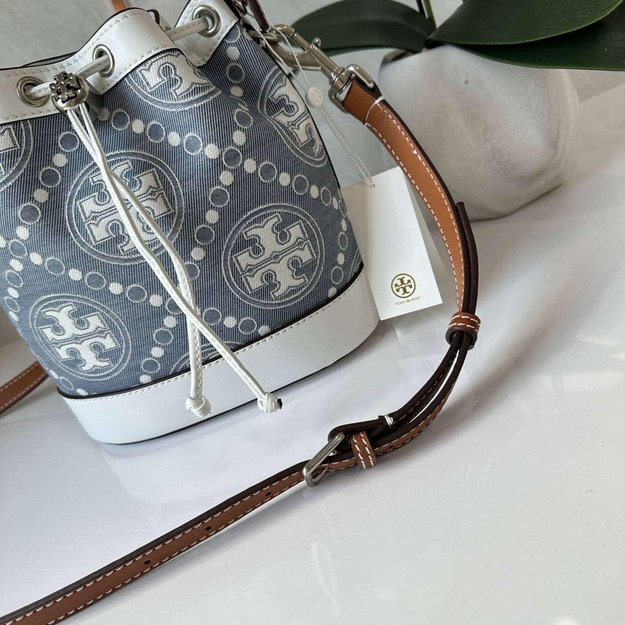 TORY BURCH T Monogram Denim Bucket Bag MEDIUM คอลเลคชั่นใหม่ รูปแบบคลาสสิค พกพาความหรูหราไปได้ทุกที่ด้วยกระเป๋าทรง Bucket ขนาดกลางและปิดด้วยเชือกรูดพร้อมโลโก้แวววาว วัสดุผ้าเดนิมแจ็คการ์ด ตัดขอบหนังแท้