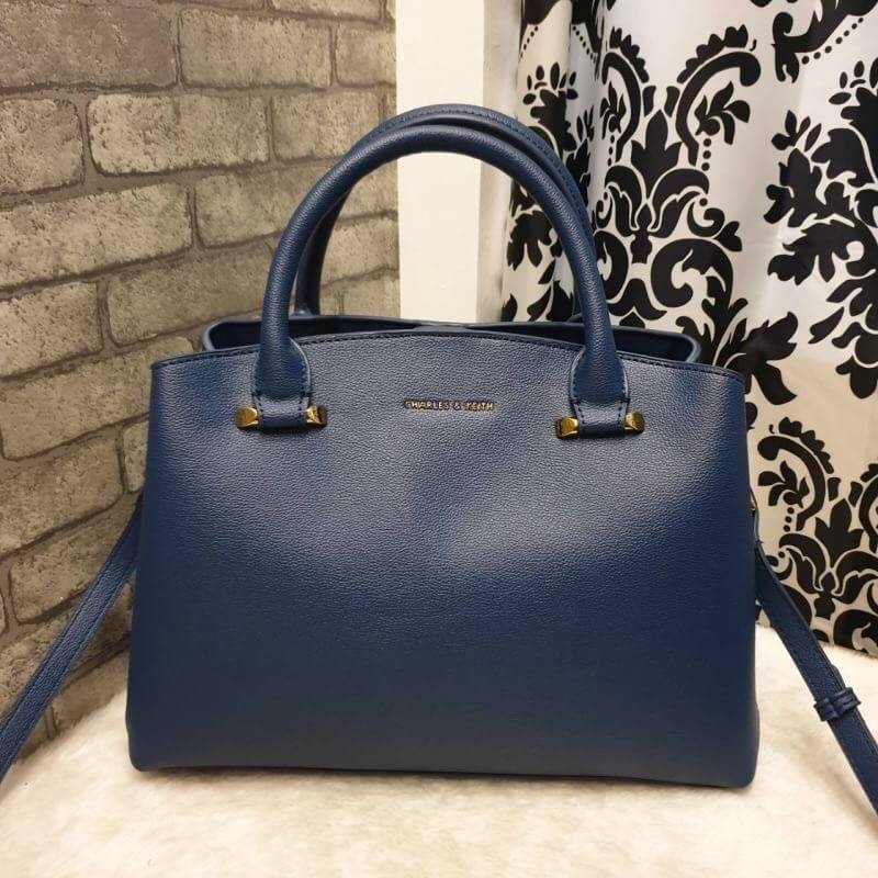 CHARLES & KEITH CLASSIC TOP HANDLE BAG กระเป๋าถือหรือสะพายใบใหญ่ ทรงแข็ง หนัง pu สวย ดีไซน์เรียบหรู ดูดี ด้านหน้าป้ายโลโก้แบบนูน ด้านหลังมีซ่องซิป 1 ช่อง เปิด-ปิดแบบกระดุมแม่เหล็ก ภายในมี 2 ช่องใหญ่ คั่นกลางด้วยช่องซิป มีหมุดรองรองฐานสี่มุม มาพร้อมสายสะพา
