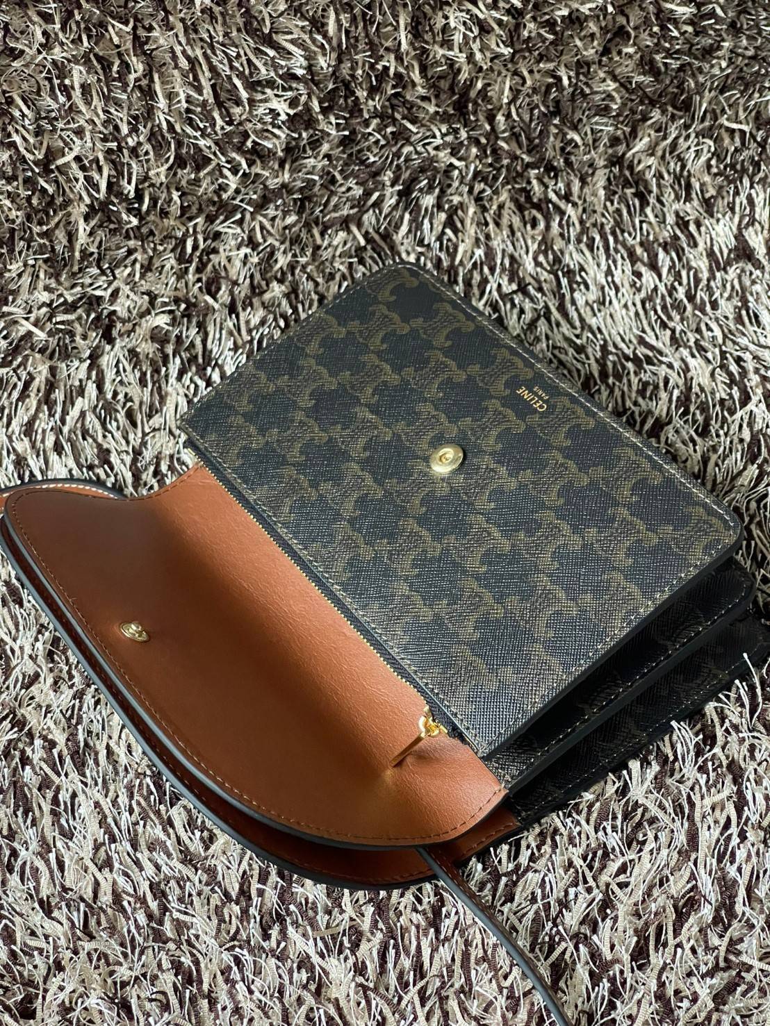 CELINE WALLET ON STRAP IN TRIOMPHE CANVAS กระเป๋าสะพายไหล่สุดเก๋ใบนี้ผลิตจากผ้าใบเคลือบอย่างดีพร้อมขอบหนังสีน้ำตาล กระเป๋ามีสายสะพายหนังสีน้ำตาลพร้อมฮาร์ดแวร์สีทอง ถอดสายออกเพื่อเป็นกระเป๋าถือทรงคลัชท์เปลี่ยนลุคช์ ลวดลายtriomphe ความเป็นแบรนด์ CELINE ได้อ