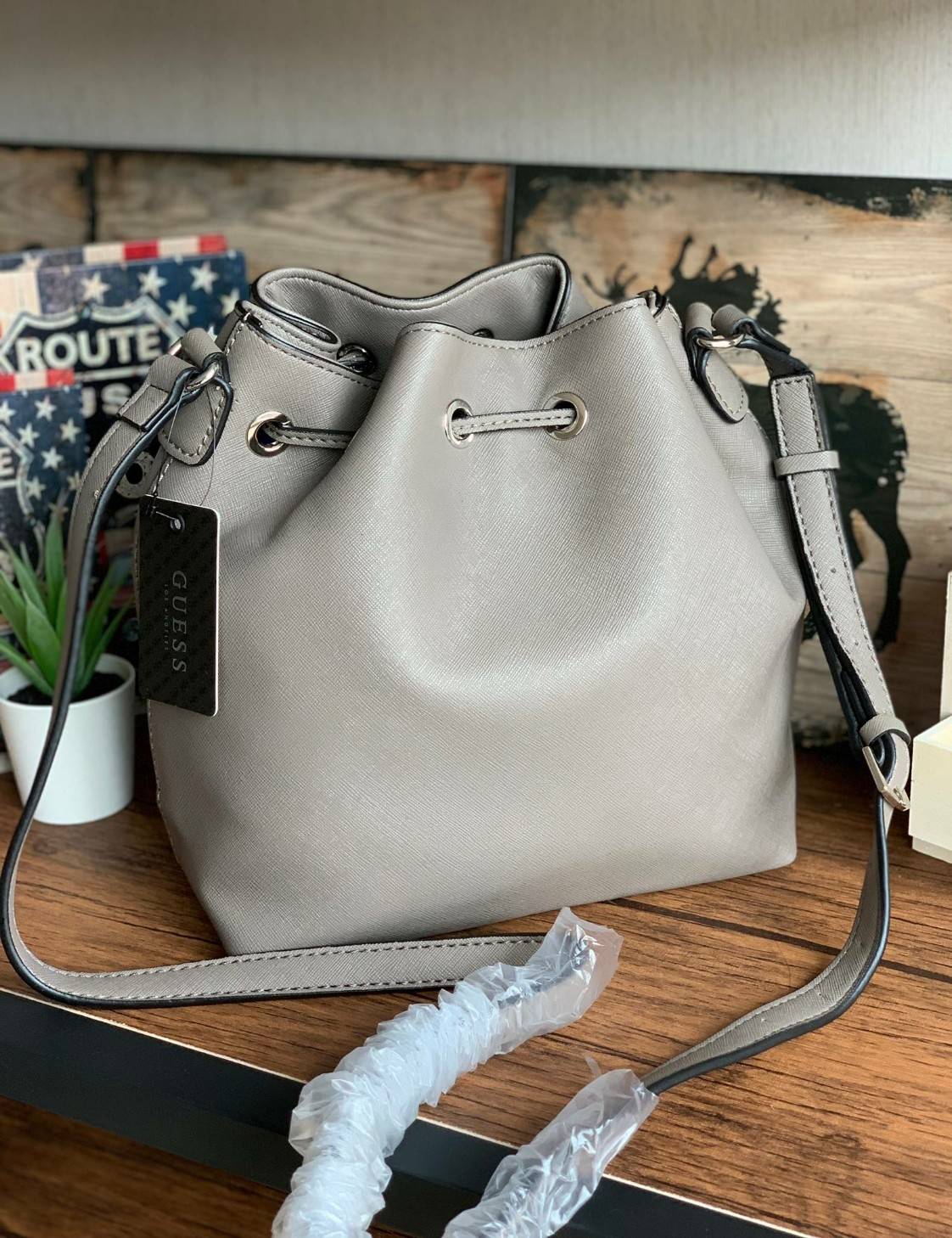 Guess Drawstring Bucket Bag กระเป๋าสะพายขนาดกลาง วัสดุลายหนังsaffiano ฐานกว้างตั้งอยู่ทรง มีซิกเนเจอร์ที่ด้านหน้าเป็นโลโก้ตัวนูน เปิดปิดแบบหูรูดและกระดุมแม่เหล็ก มีช่องใช้งานหลายข่อง สายสะพายปรับได้แบบเข็มขัด สวยแบบมีดีเทลเก๋ๆ สะพายเที่ยวระหว่างวันได้สบาย