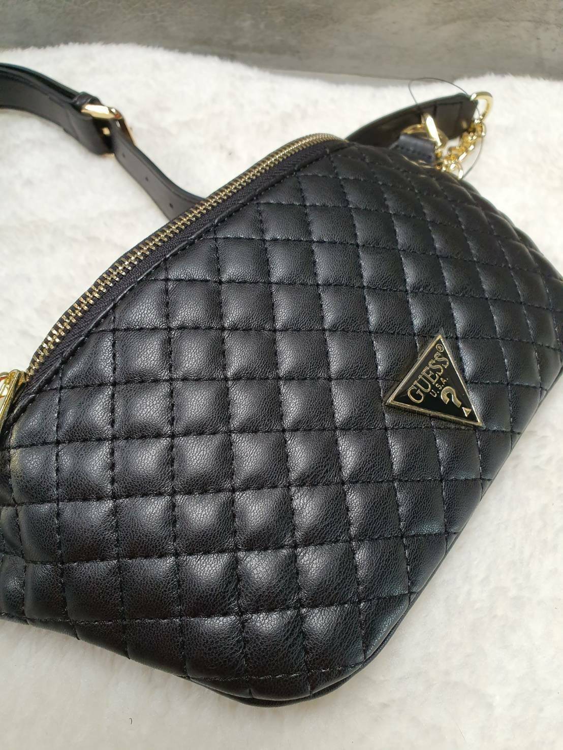 กระเป๋า Guess รุ่นนี้คาดเอว/คาดอก/สะพายข้างได้ครบทุกฟังก์ชั่น ด้านหน้าหนังเป็นลายตาราง ติดโลโก้แบรนด์รูปสามเหลี่ยมด้านหน้า เปิดปิดด้วยซิปยาว ด้านในเป็นช่องกว้างมีช่องซิปด้านใน ตัวกระเป๋าด้านหลังเป็นหนังเรียบ รุ่นนี้มีสายสะพายมา 2 เส้น เส้นแรกเป็นสายหนังปร